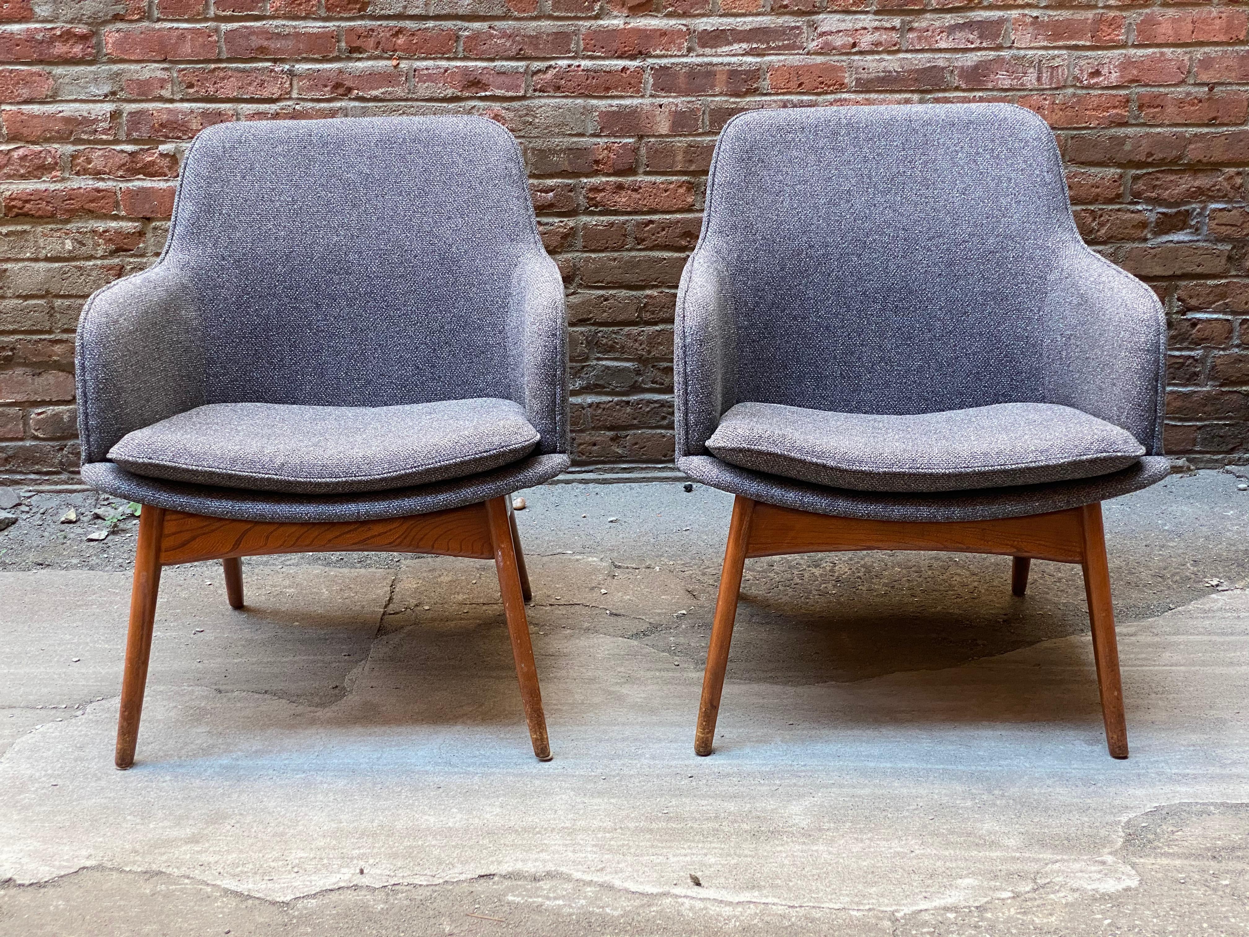 A wonderful pair of streamlined Mid-Century Modern lounge chairs. Re-upholstered in a dark gray nubby fabric. Featuring a cozy contoured shape, bow tie stretcher base with tapered wood legs, circa 1950-1960. Original finish to