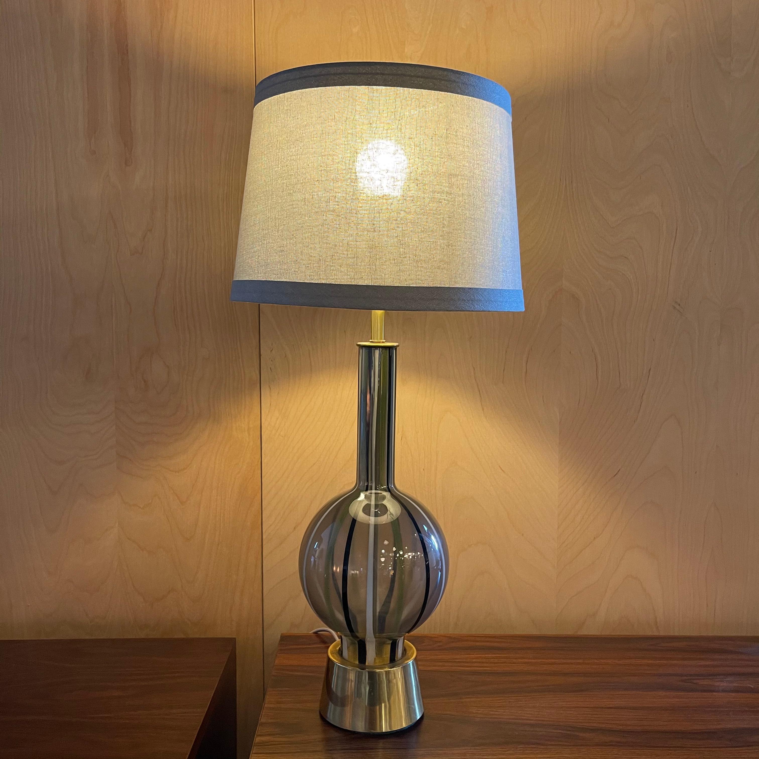 Mid-Century Modern table lamp features a striped glass, genie bottle base with brass-plated metal accents. The lamp shade 10-13 diameter x 9 ht inches, clips to the bulb. The overall height with the shade is 27 inches.