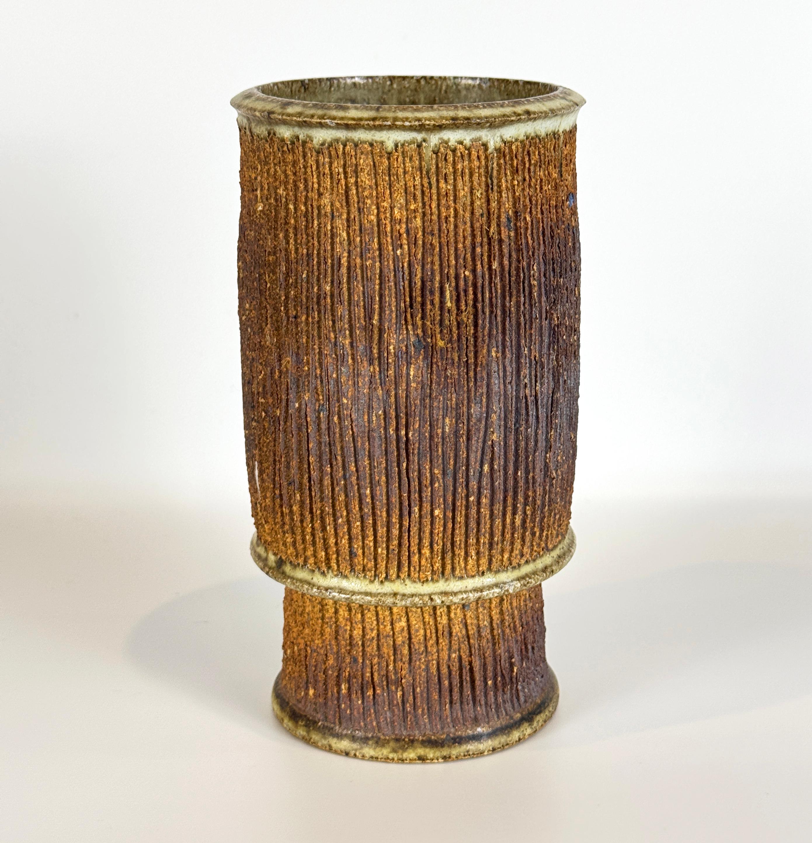 Vase en céramique de studio du milieu du siècle dans un style brutaliste. De forme cylindrique et reposant sur un pied haut, ce vase merveilleusement texturé est décoré de coupes verticales profondément incisées sur l'ensemble du corps grossièrement