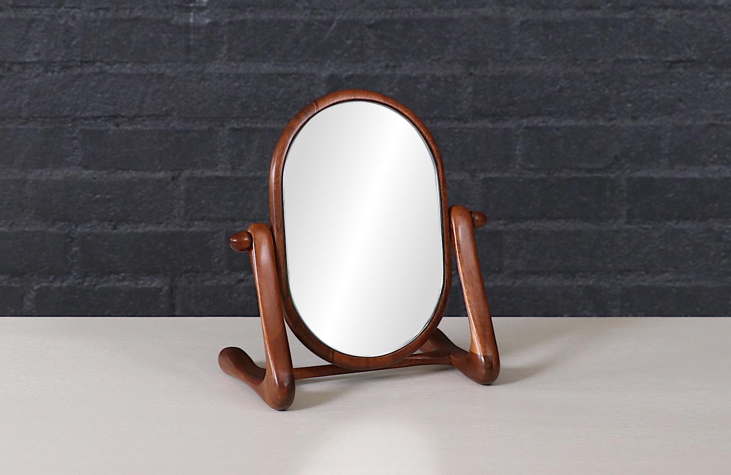 This beautifully sculpted Mid-Century Modern vanity mirror, crafted in the United States during the 1960s, is a stunning example of organic design. Made from solid walnut, it features a gracefully curved frame and an elegantly sculpted base, giving