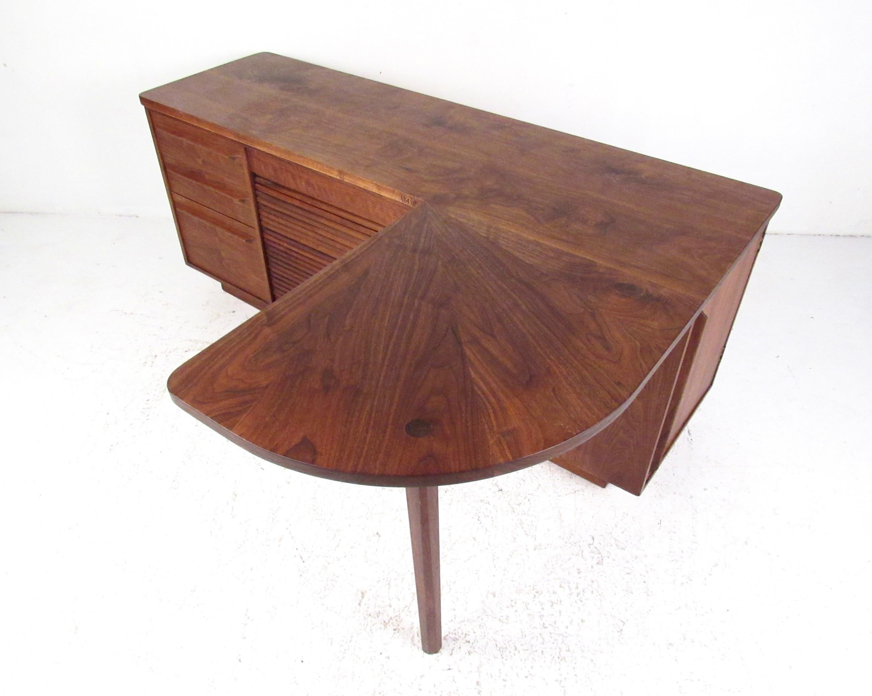 This unique L shaped executive desk features spacious work space, vertical tambour door cabinet, carefully carved handles, and plenty of storage options for home or business office. The quality mid-century modern construction of this American made