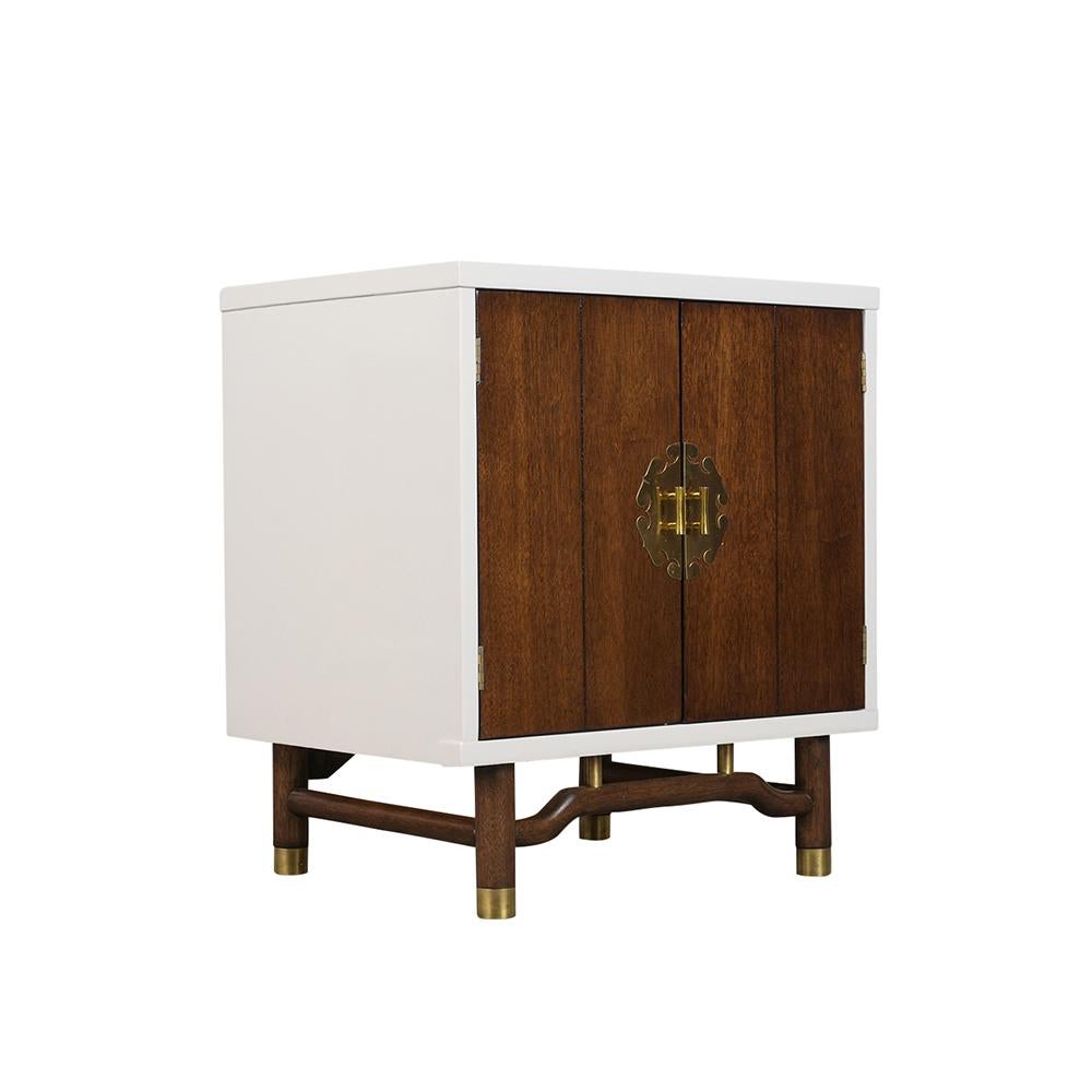 This pair of Mid-Century Modern-style nightstands are made out of walnut wood and has a rich walnut and white stained color combination with a lacquered finish. The nightstands feature two wooden doors with oriental style brass plate and handle