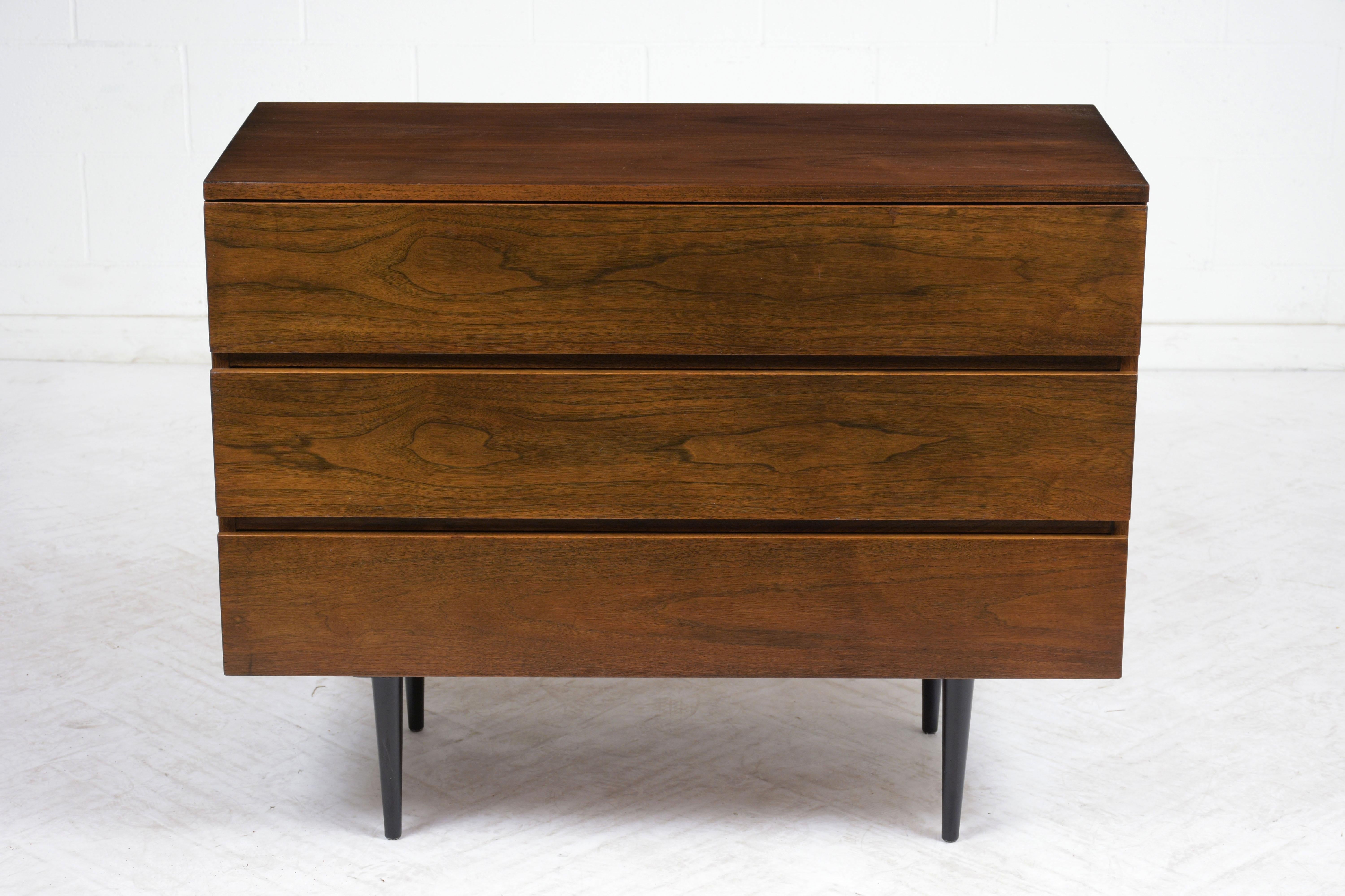 This 1960s Mid-Century Modern style chest of drawers has been completely restored. The chest is a rich walnut color with a lacquered finish. There are three drawers that open with finger notches. The chest is finished with tapered legs finished in a
