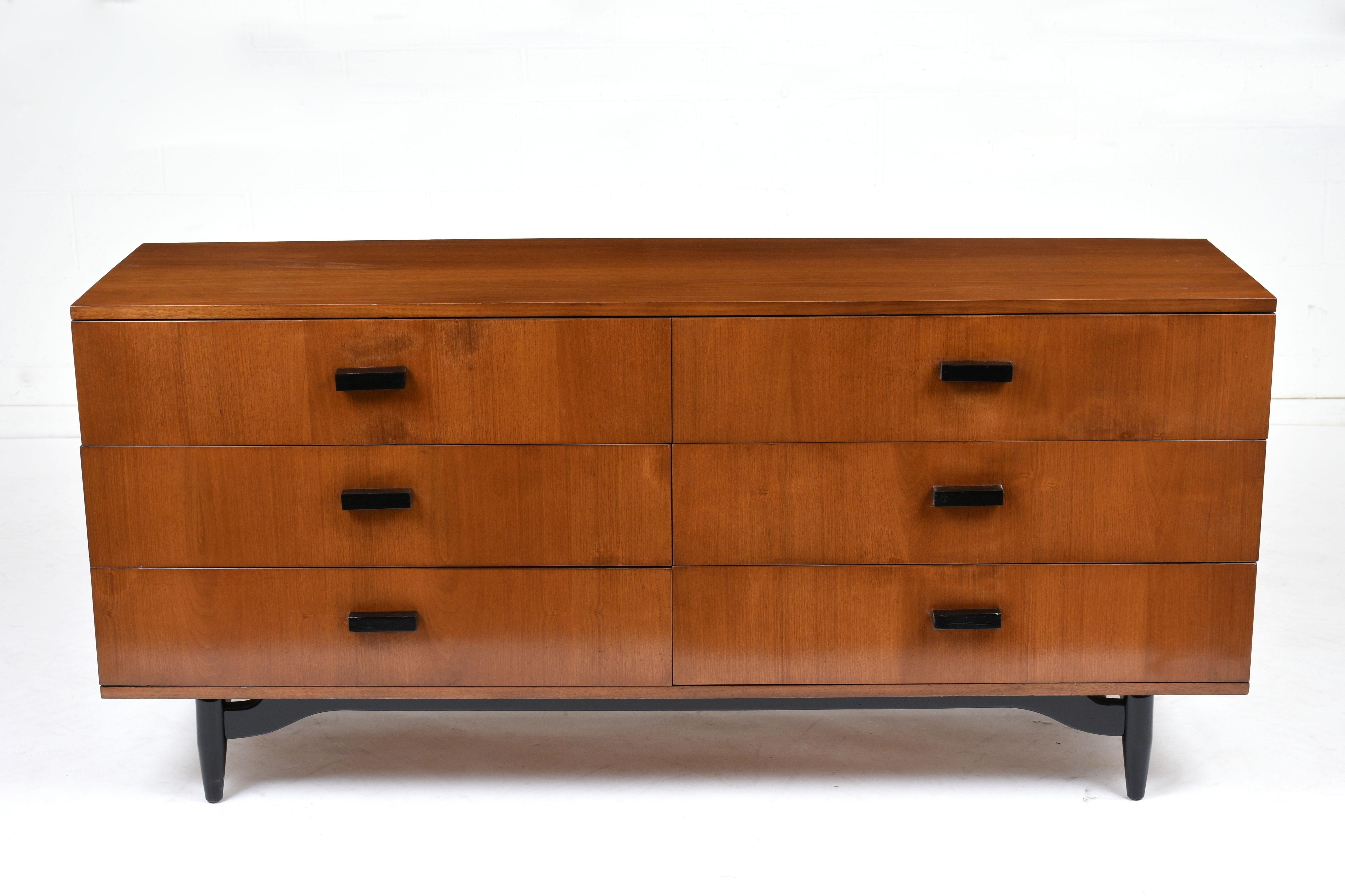 This 1960s Mid-Century Modern style chest of drawers is stained in a light walnut color and black color with a lacquered finish. This chest featured six drawers with ample storage space and carved wood handles finished in black color. The Chest is