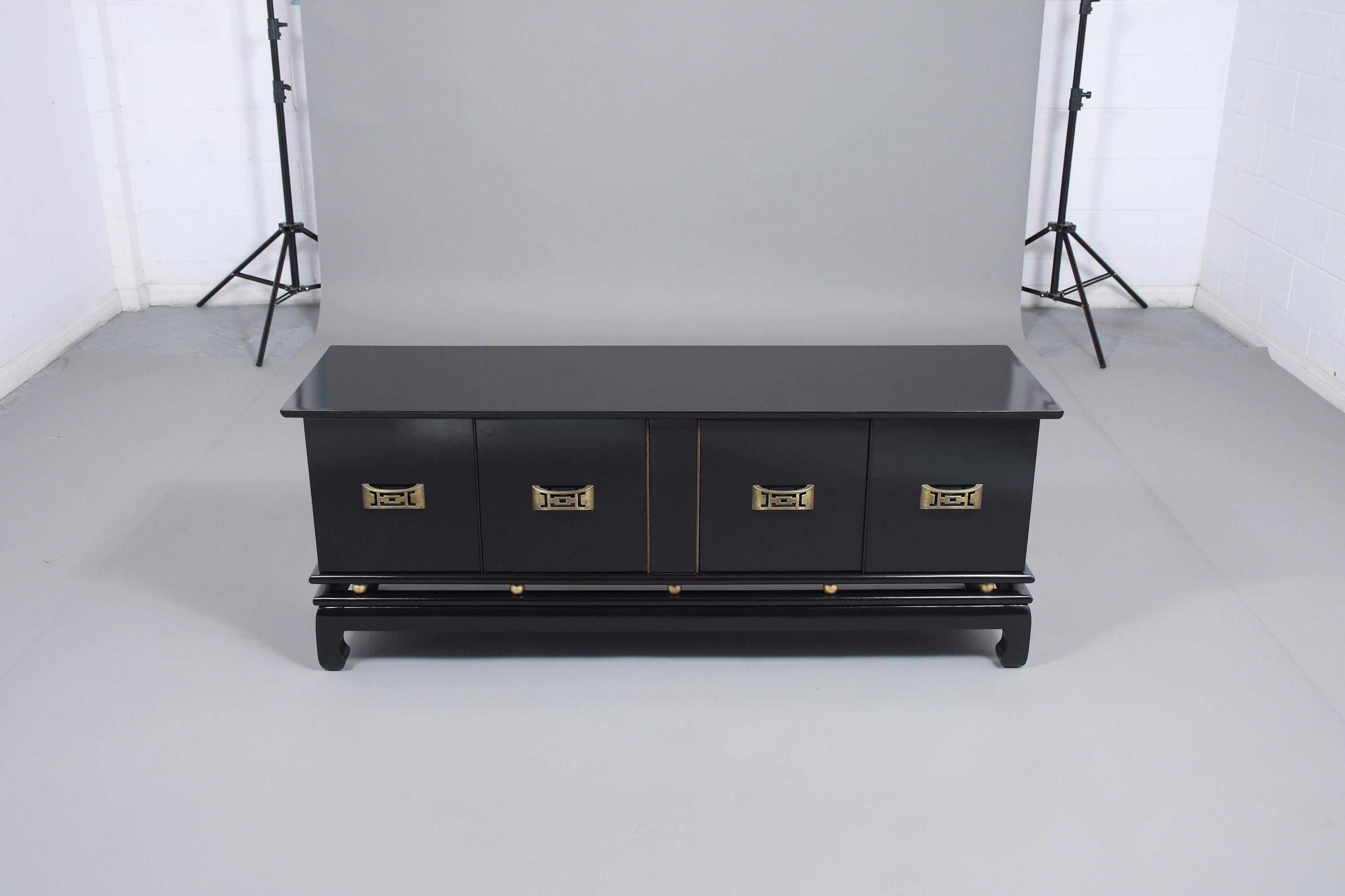 This vintage low mid-century modern credenza has been newly restored and features a newly ebonized lacquered finish. The cabinet comes with four cabinet doors with unique brass handles, two large interior shelves for additional storage, and rests on