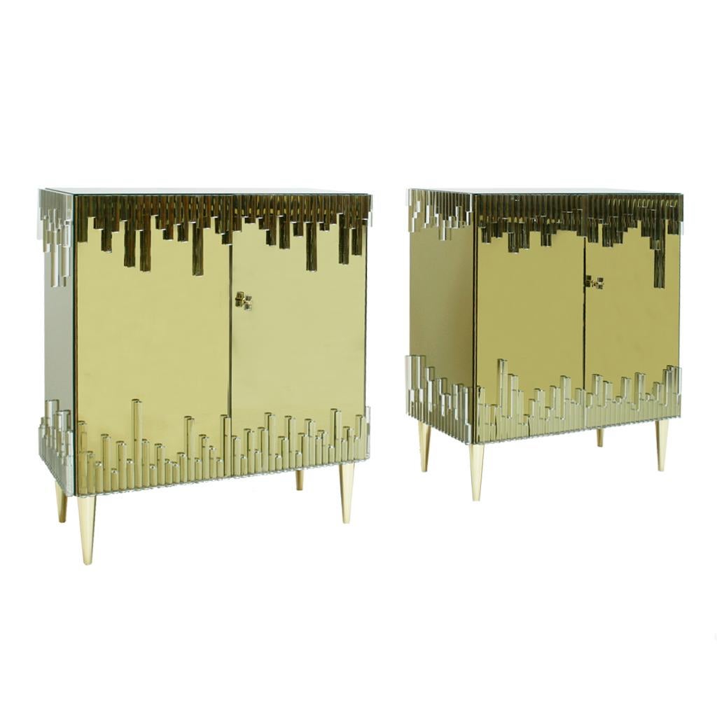 Midcentury style pair of Italian sideboards. Structure made of solid birch wood covered with golden mirror and cylinder glass details on top and bottom of the surface. Composed of two folding doors with one shelve inside and brass legs.

Our main