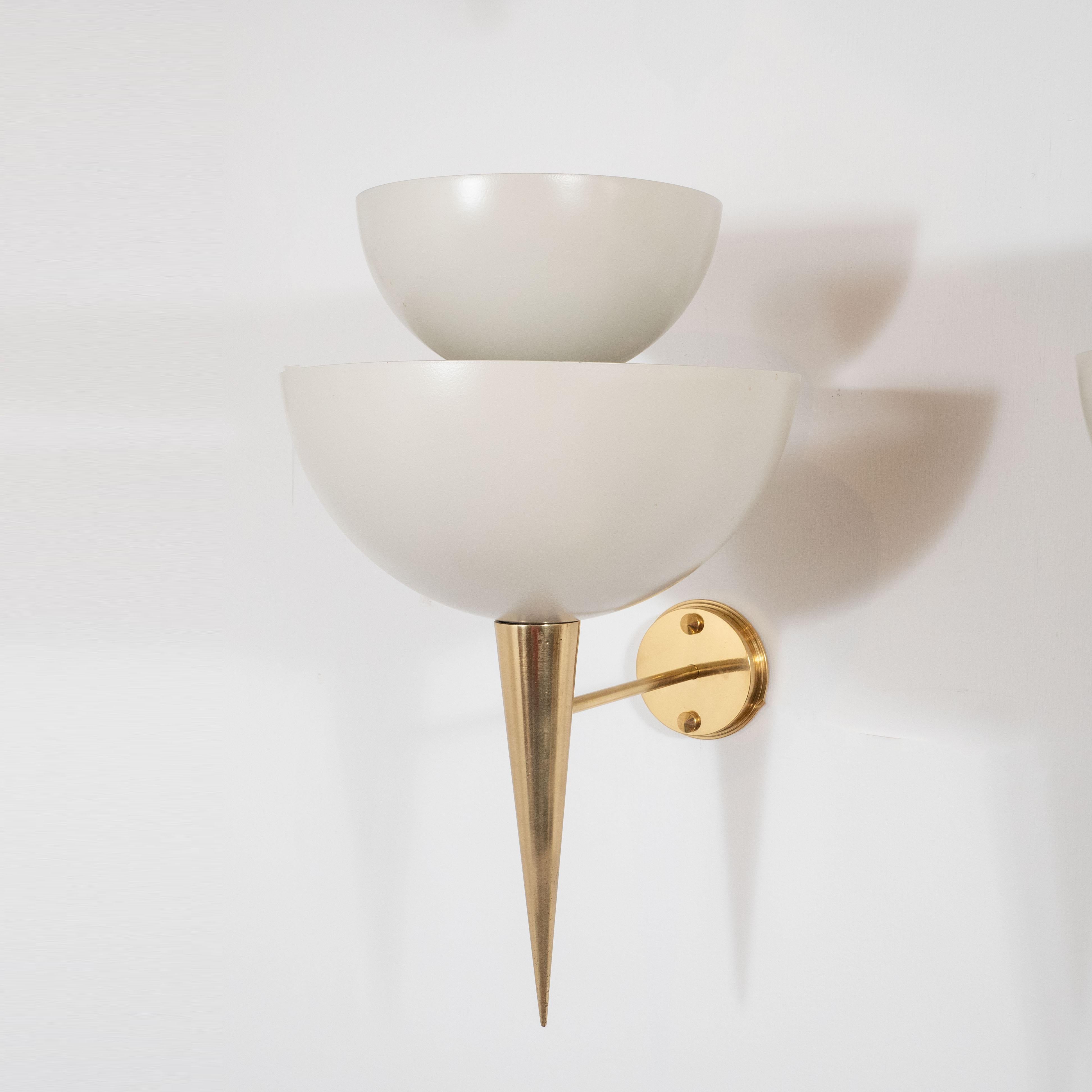Inspired by Mid-Century Modern design, this pair Italian-made wall sconce consists of two tiers of soft white powder-coated metal cups that sit atop a polished brass pointed finial, sconce is attached to a brass wall plate. The natural brass will