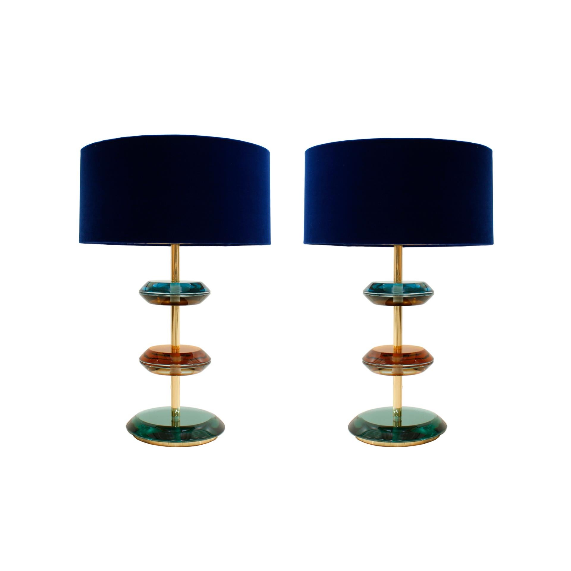 Paire de lampes de table conçues par I.A. Studio. Comprend une structure en laiton massif ornée de pièces en verre coloré de Murano. Fabriqués en Italie, ils sont complétés par des abat-jour circulaires en laine bouclée blanche.

Dimensions avec