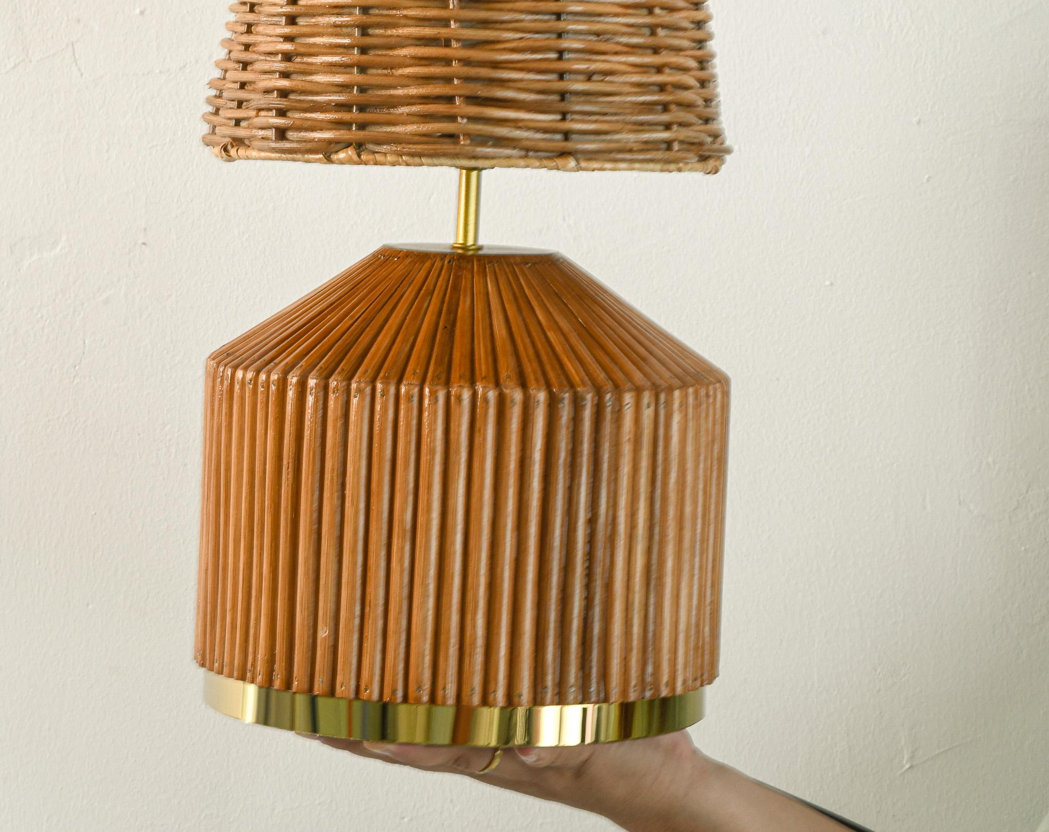 Lampe de table en rotin de style classique et moderne du milieu du siècle. La base est méticuleusement fabriquée à la main afin d'obtenir de belles lignes de rotin en roseau et est finie avec des accents dorés pour une touche luxueuse. La forme