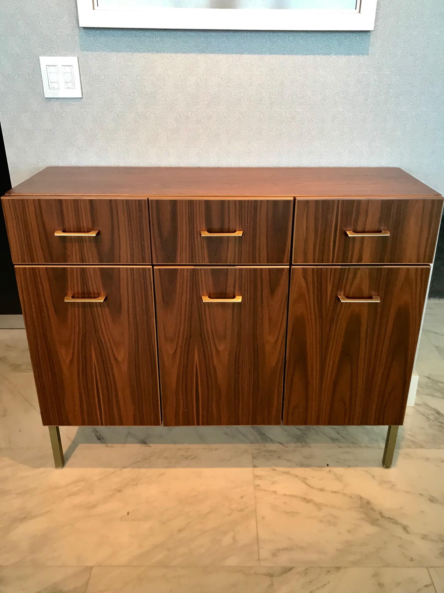 Custom modernist cabinet in bookmatched walnut wood with satin brass hardware. Elegant streamline design fitted with long double drawer and with single drawer on the top portion. Cabinet doors open to reveal interior storage with adjustable