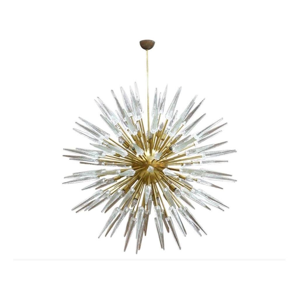 An impressive and very large Sputnik chandelier made of clear Murano glass shards and brass rods fixed to a central brass lacquered orb. Bulbs are coming from the brass rods ends and hidden between the hallo of glass spikes. Made in Italy.

Every