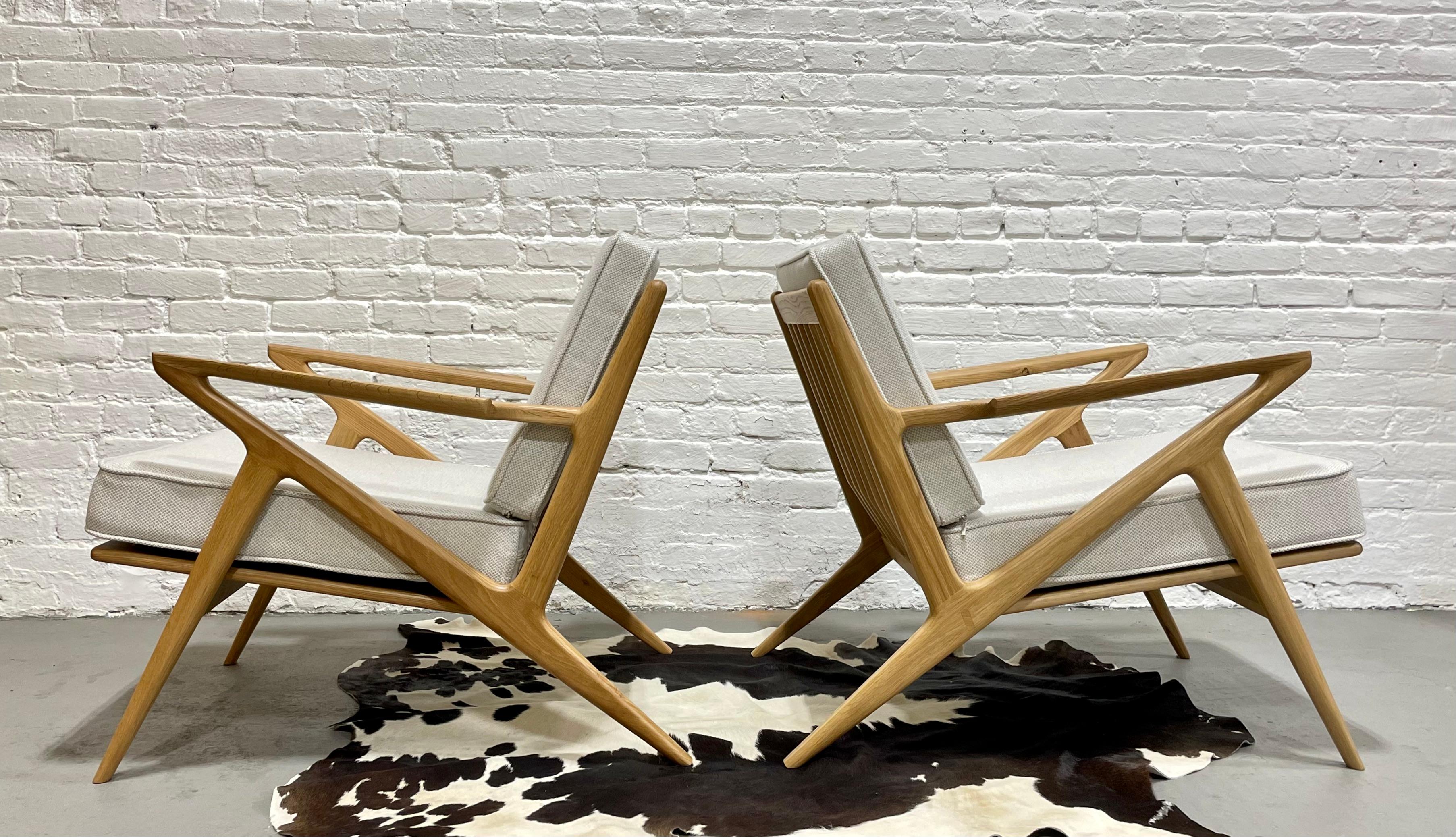 Pair of Mid-Century Modern styled lounge chairs, intricately handcrafted and designed in solid oak. This incredible set offers loads of design details such as sculptured armrests, triangular back slats and stunning wood grains. The cushions are high
