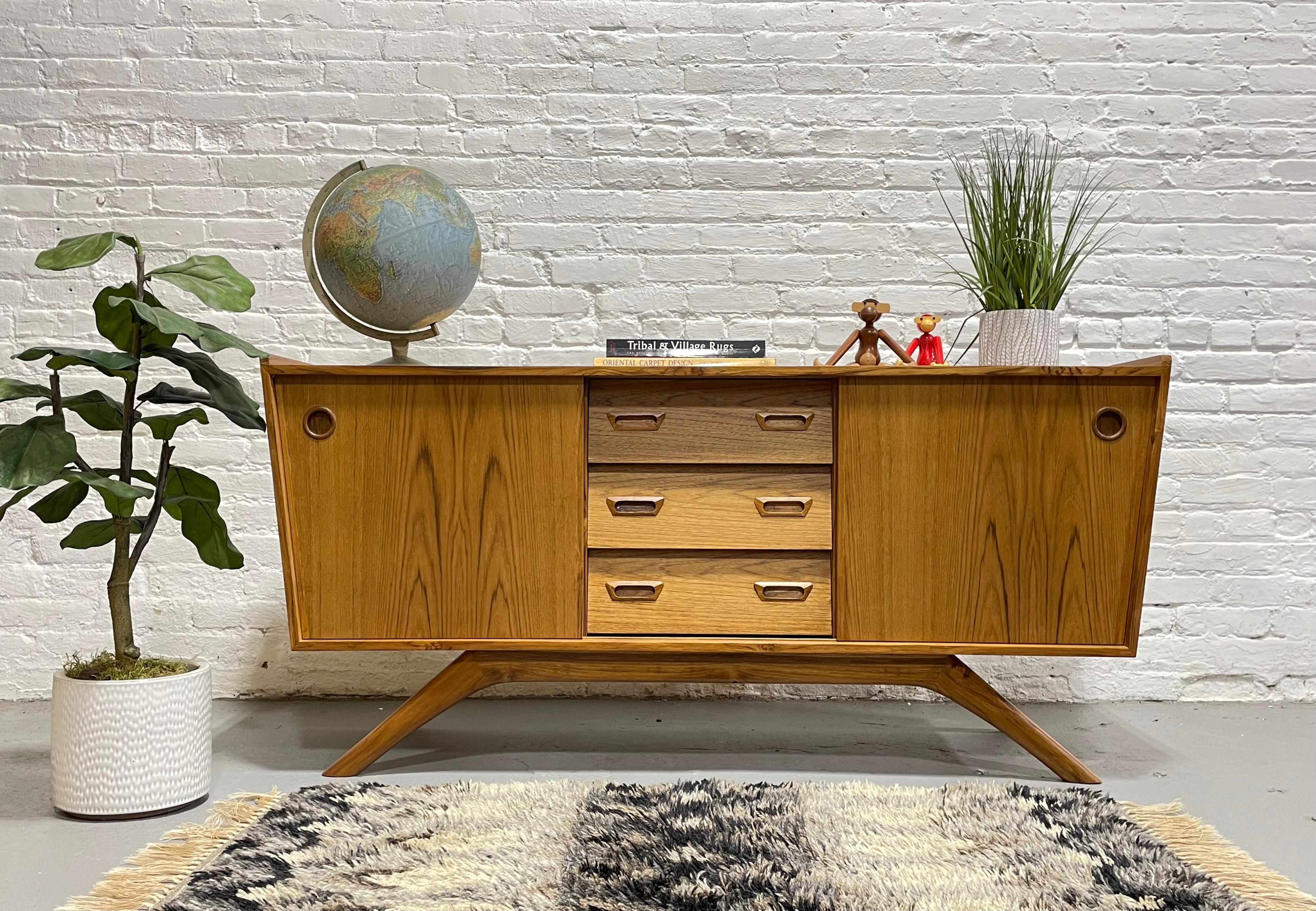 Mid Century Modern Asymmetrical handmade Teak credenza / media stand featuring a low height and sexy splayed leg design. This gorgeous piece has incredible design details, from its unique splayed leg design to its asymmetrical case and angular