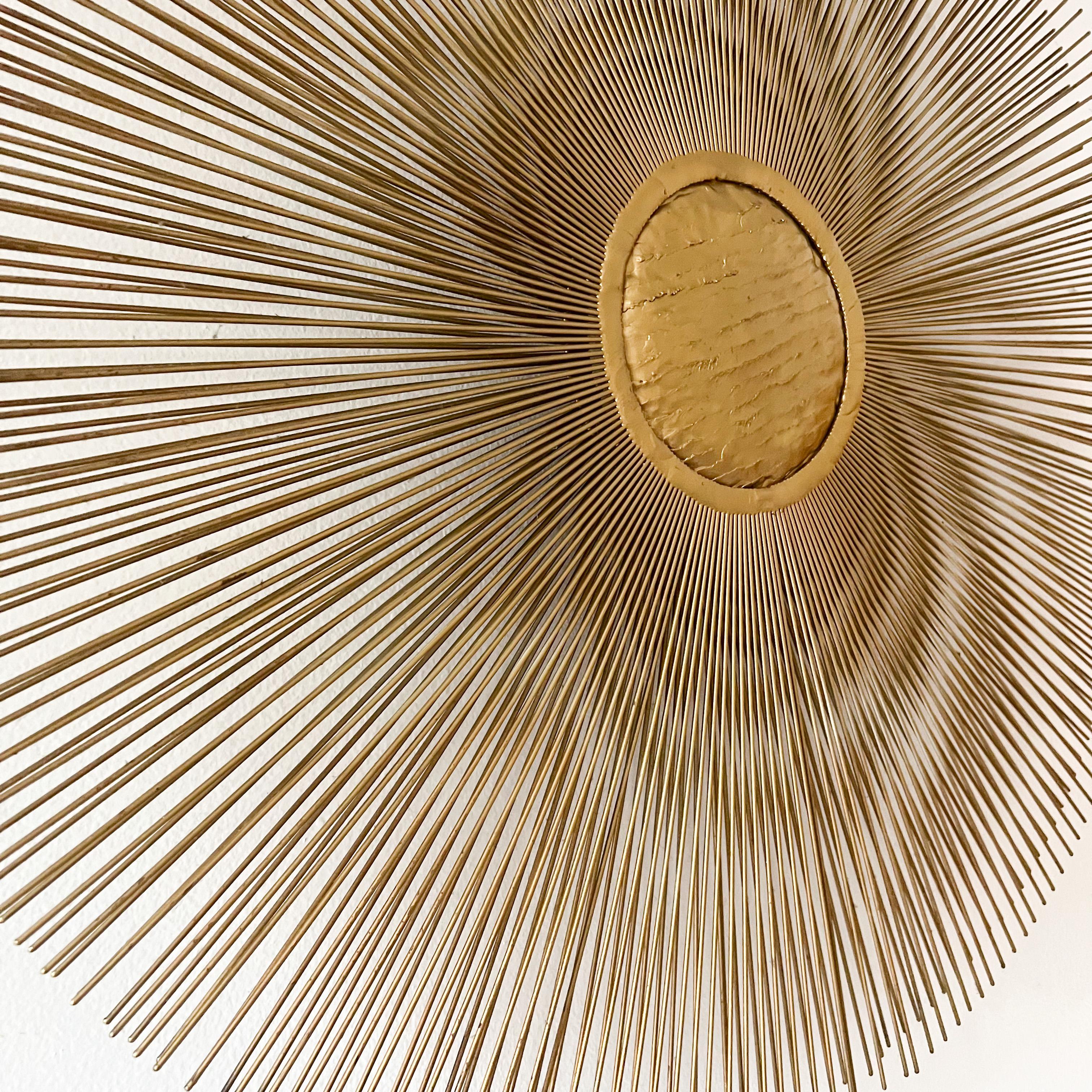 A must have midcentury icon sunburst wall sculpture designed and crafted by Casa Devall in the United States, circa 1970s. Our sculpture features a textured brass center and two layers of painted rods, creating a unique sunburst effect like an