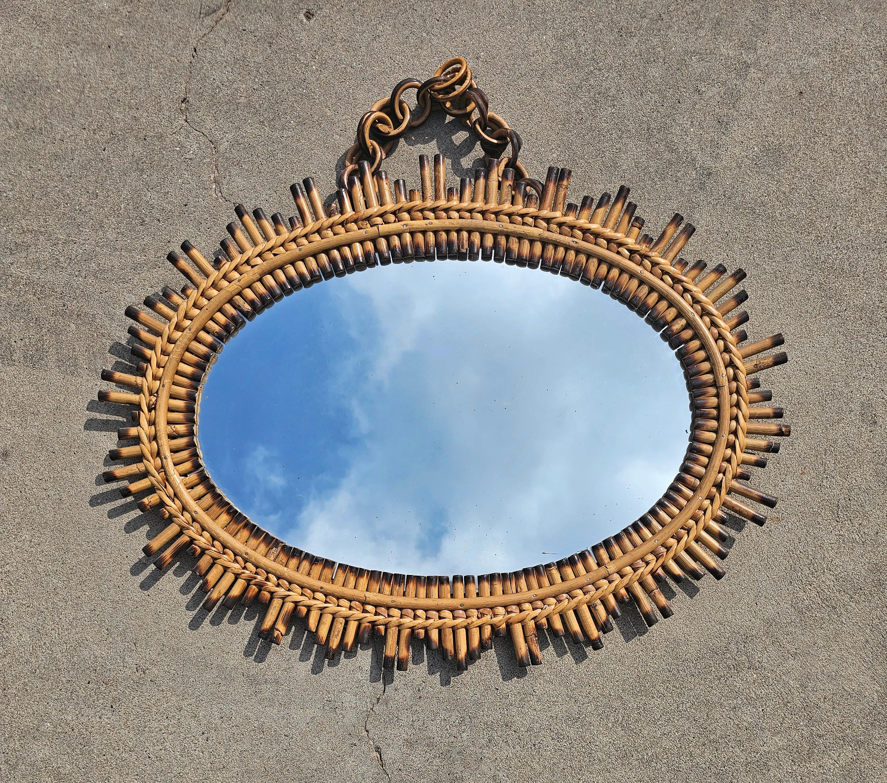 In this listing you will find a unique oval Mid Century Modern Sunburst Mirror. The frame of the mirror is done in bamboo, with burnt tips, giving it striking look. The mirror is wall mounted, with equally striking chain made of rattan. Made in
