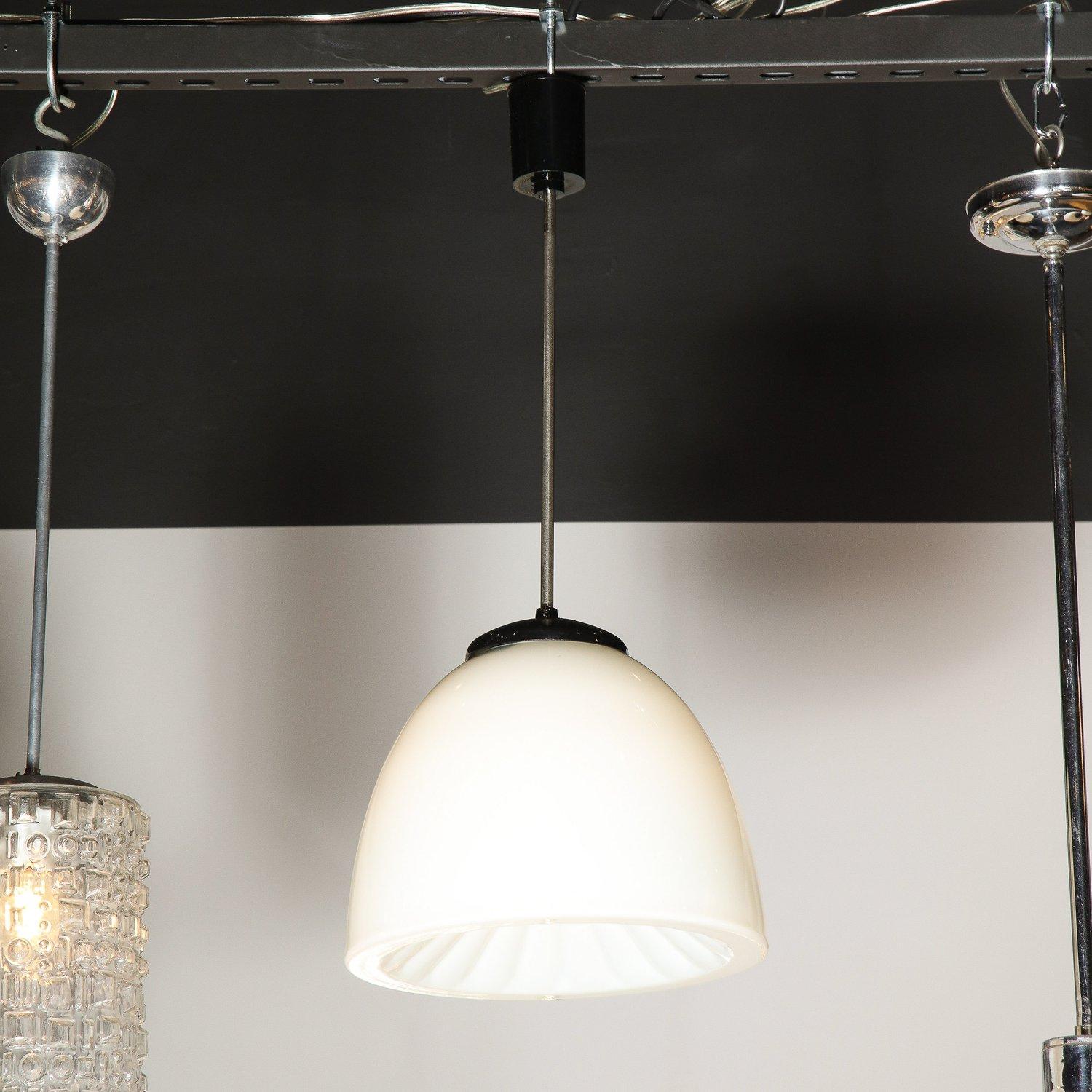 These refined and understated Mid-Century Modern pendants were realized in the Czechoslovakia, circa 1950. They feature a sculptural domed shade in opaque milk glass with dramatically concave sunburst interior striated with a wealth of channeled