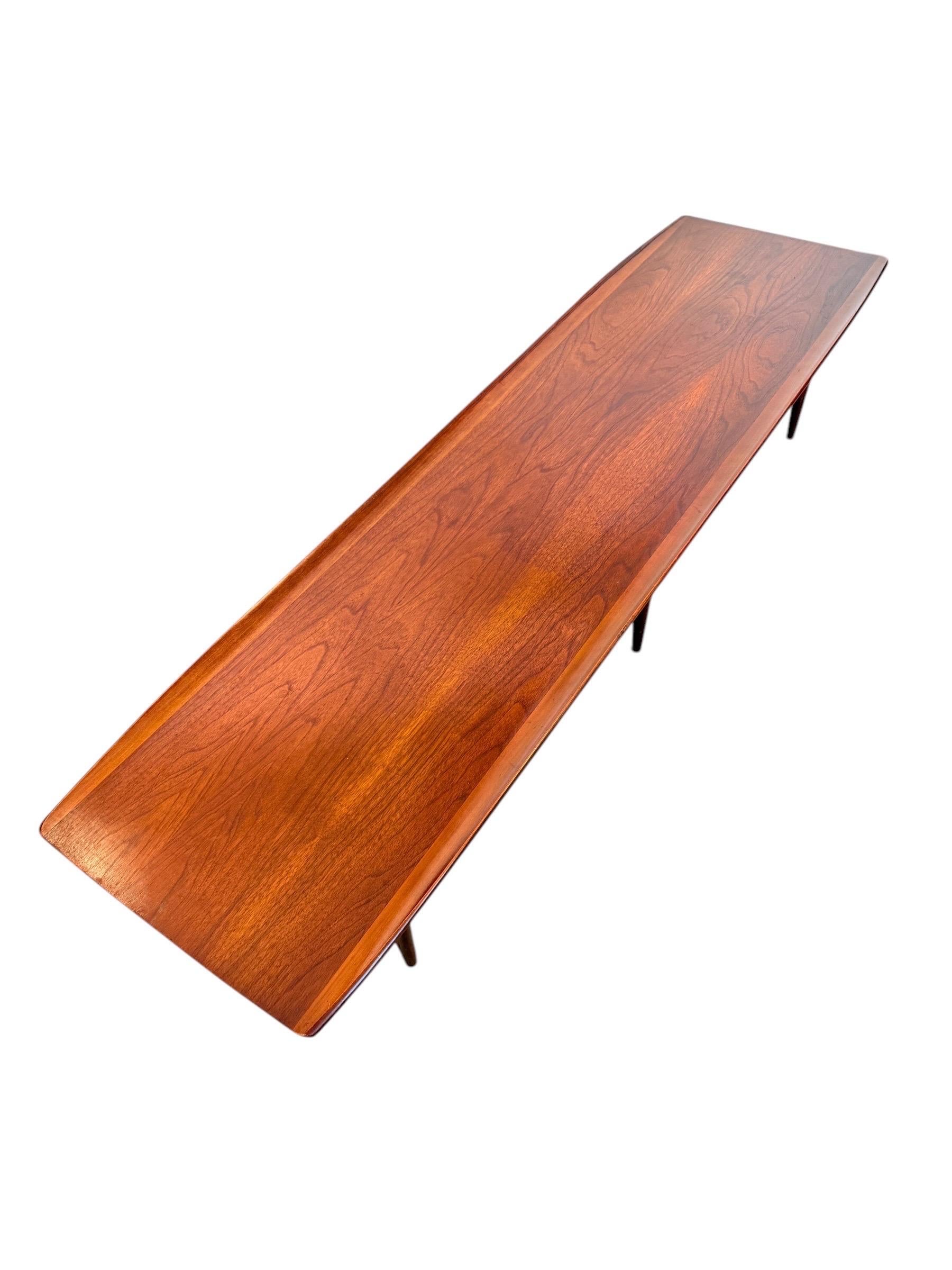 This striking mid-century surfboard coffee table by Bassett Furniture is a timeless piece from the 1960s “Artisan” line, attributed to designer Leo A. Jiranek. Crafted in solid black walnut, the table features a long, sculpted profile with a