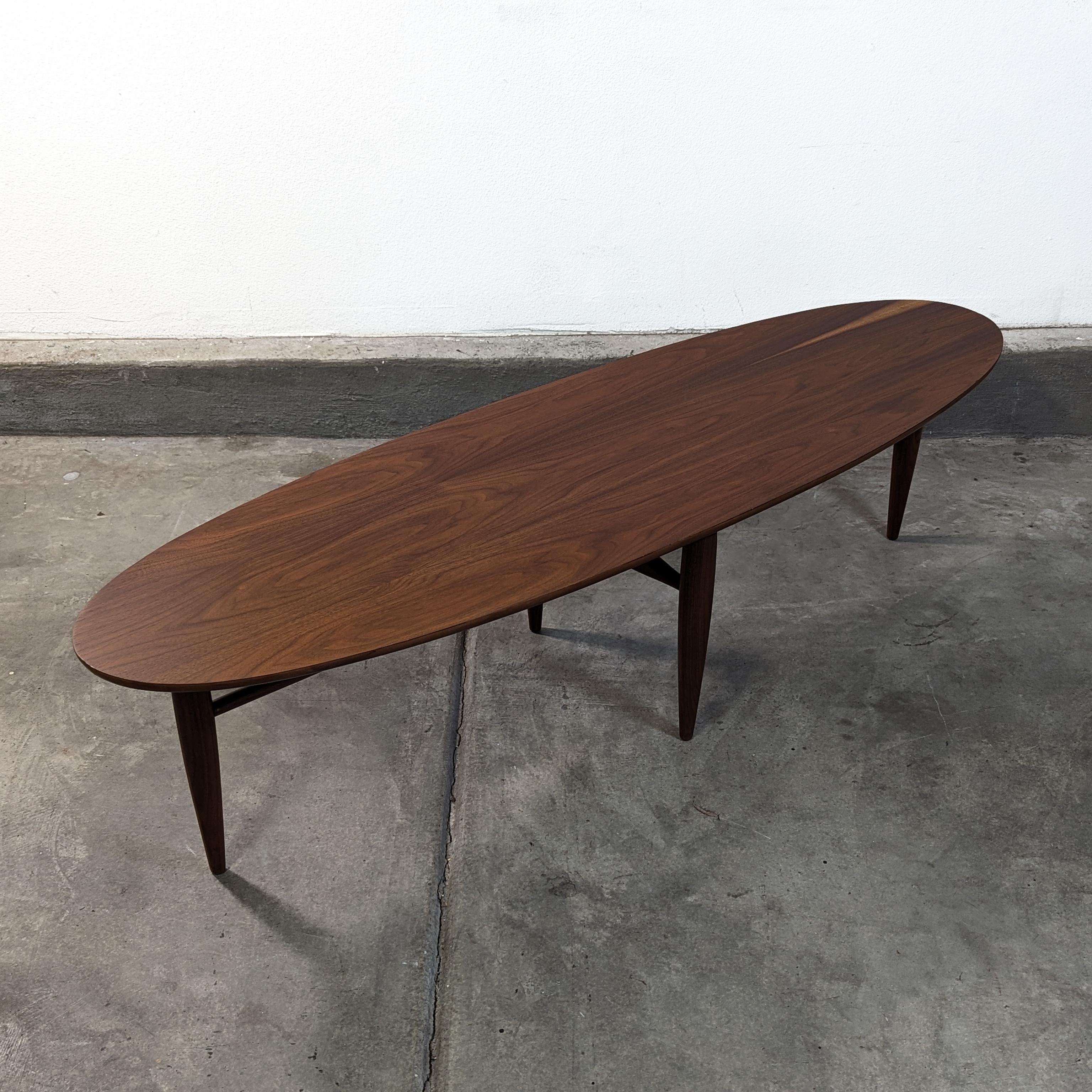 Embrace the timeless elegance of mid-century design with this exquisite vintage Surfboard Coffee Table by Mersman, circa 1960s. Meticulously refinished to showcase its sleek lines and beautiful wood grain, this piece is a stunning representation of
