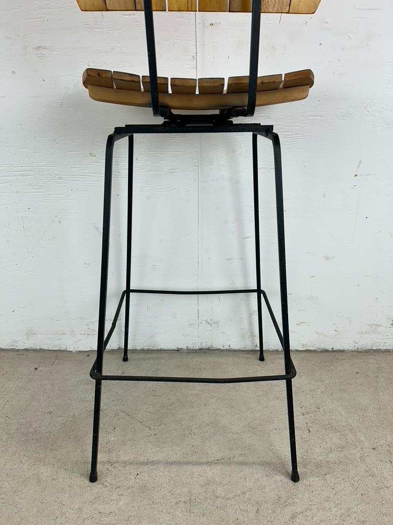 Ce tabouret de bar moderne du milieu du siècle dans le style d'Arthur Umanoff présente une assise et un dossier en bois courbé avec une finition originale sur une base en métal peinte en noir et pivotante.
u2028Dimensions : 16.75w 16d 40.25h