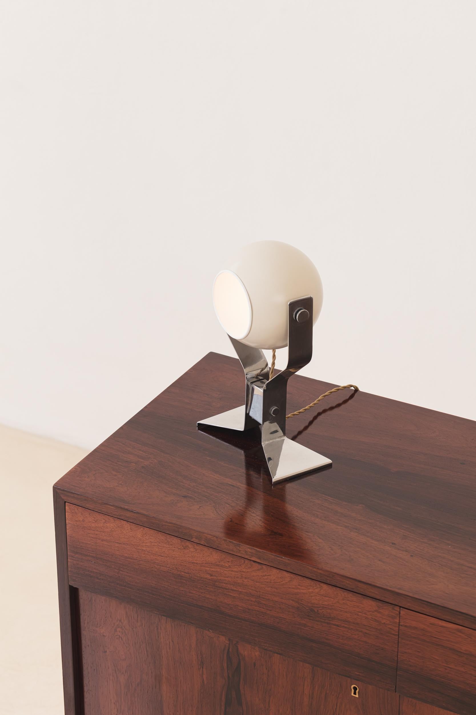 La lámpara de sobremesa diseñada por Enrico Furio para Dominici en los años 70 es una sorprendente síntesis de elegancia de mediados de siglo y refinamiento industrial. Fabricada en aluminio y latón, la lámpara presenta un esbelto soporte tubular de