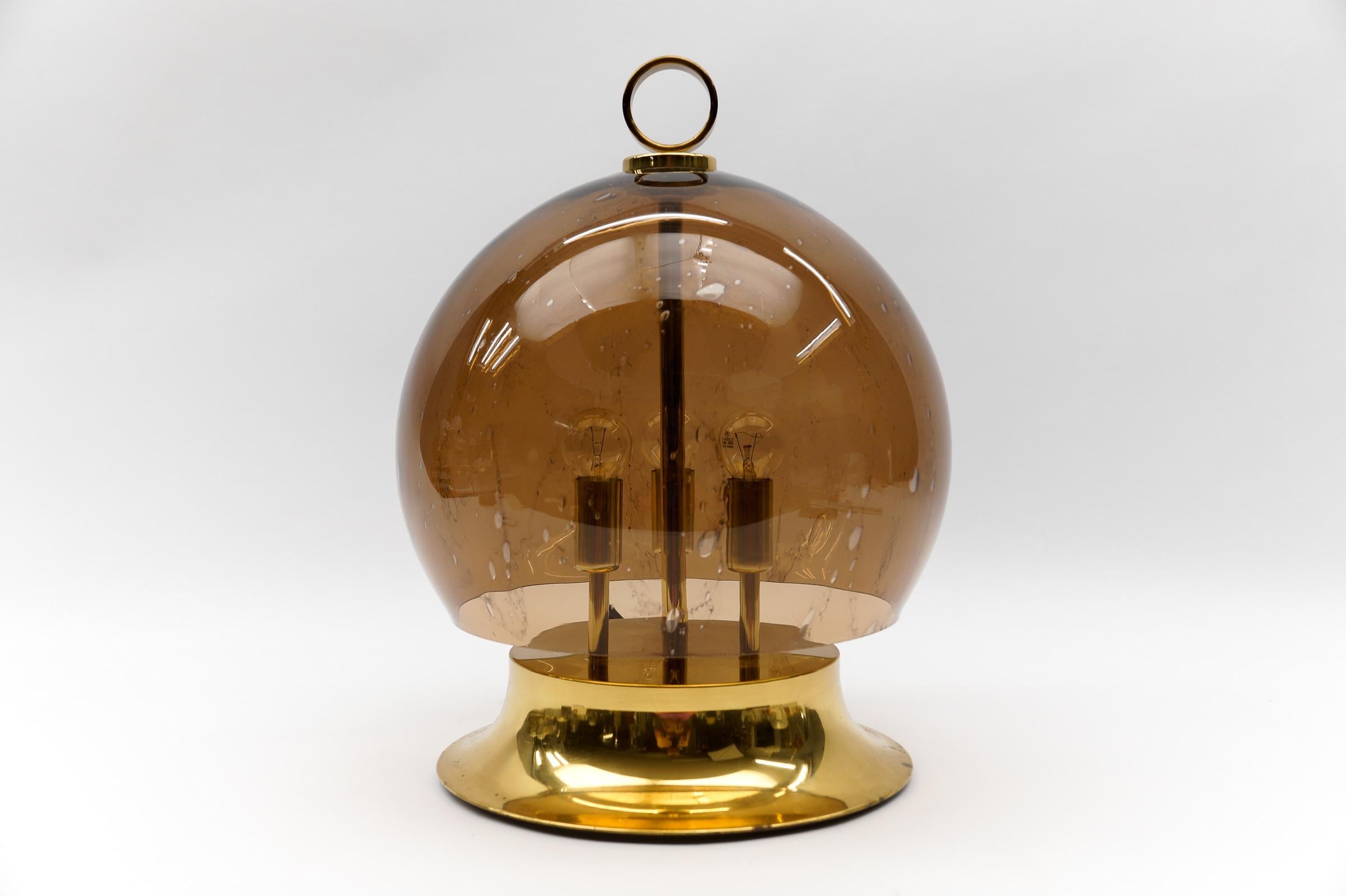Mid-Century Modern Table Lamp made in Brass and Glass, 1960s

This golden table lamp features a mouth-blown smoked glass globe.

Dimension
Height: 21.25 in (54 cm)
Diameter: 17.71 in (45 cm)

The lamp needs 3 x E14 / E15 Edison screw fit bulb, is