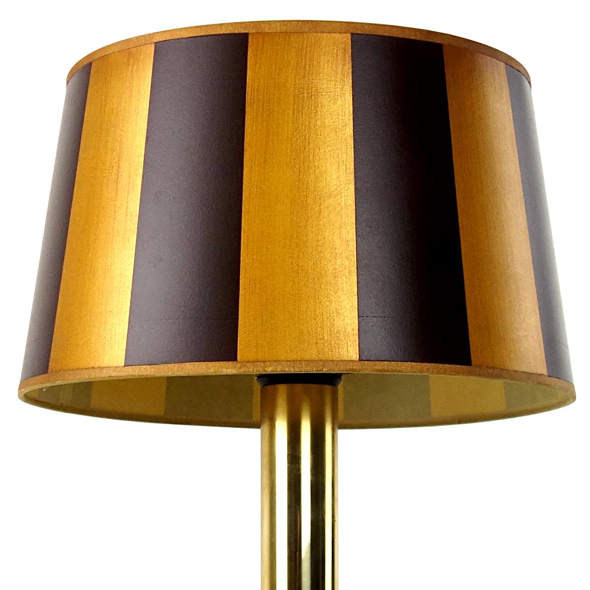 The base of this table lamp by German light specialist Doria Leuchten is made of smoked glass. It contains three bulbs, providing for dramatic lighting. There is another bulb underneath the striped shade. 
This lamp has many opulent brass accents.