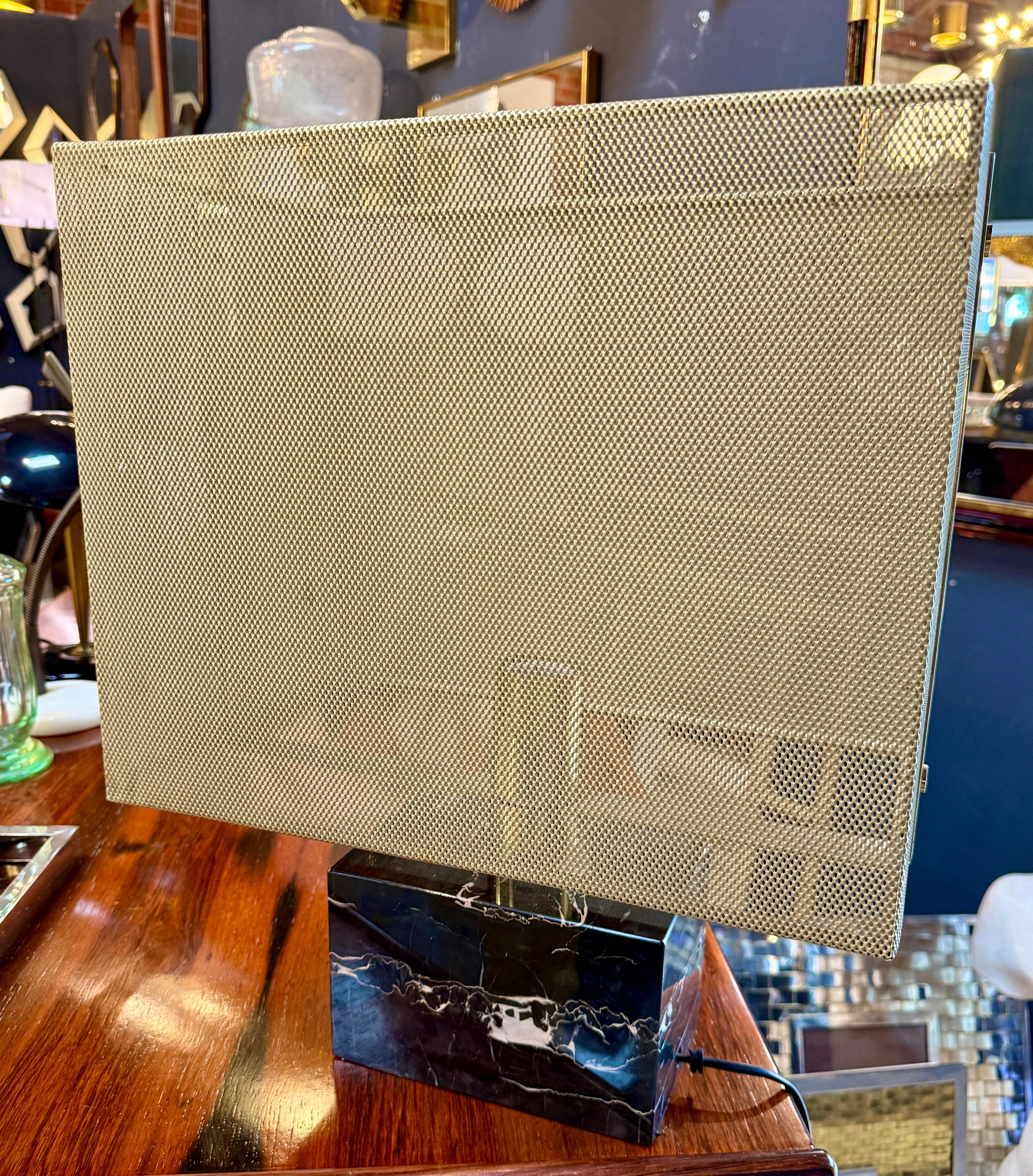 This striking mid-century modern table lamp features a bold geometric design that blends elegance with industrial flair. The rectangular shade is crafted from perforated brass mesh, allowing light to diffuse softly while creating a warm, golden