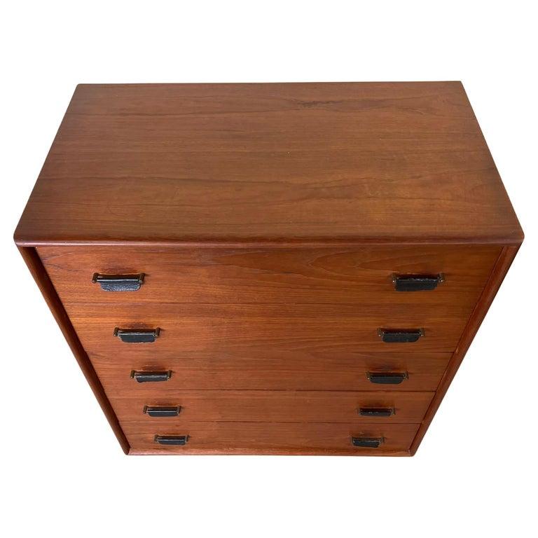 Comò alto a 5 cassetti in teak del Mid Century The Scandinavian Modern con tiretti in pelle e base a zoccolo in lacca nera. Comò in teak molto particolare con maniglie in pelle appese. Cassetti in legno massiccio con incastri a coda di rondine.
