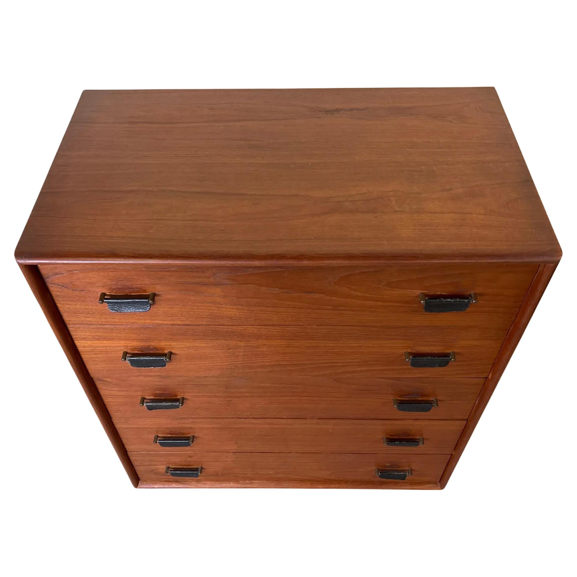 Cómoda alta de 5 cajones de madera de teca moderna escandinava de mediados de siglo, con tiradores de cuero y base de zócalo lacada en negro. Cómoda de teca muy singular con tiradores de cuero colgantes. Cajones de madera maciza con juntas de cola