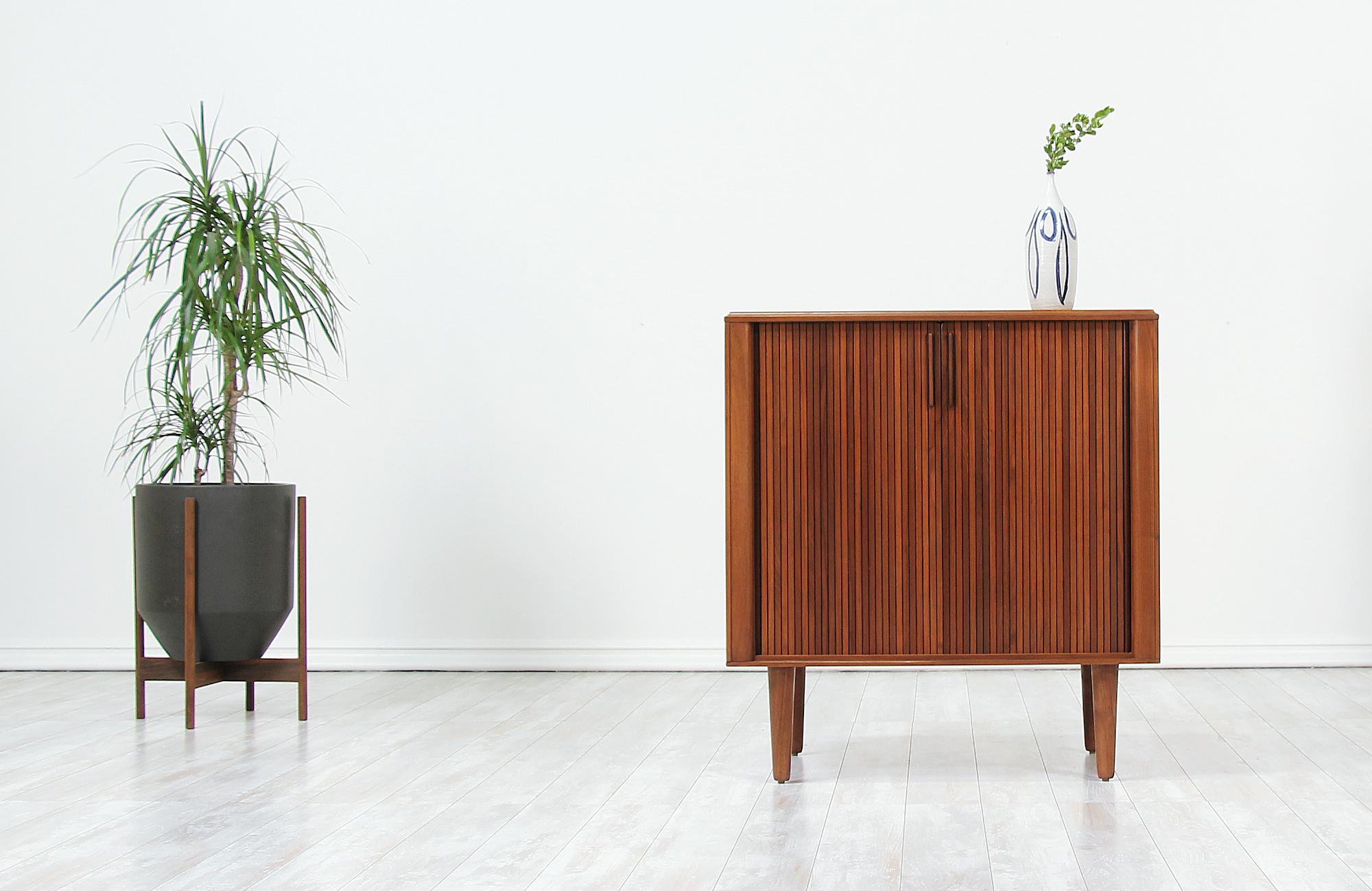 Minimalist vintage cabinet designed and manufactured in the United States by Barzilay circa 1960s. Low in profile and compact in size, this stylish cabinet features a sturdy walnut wood frame with two tambour doors and four tapered legs that