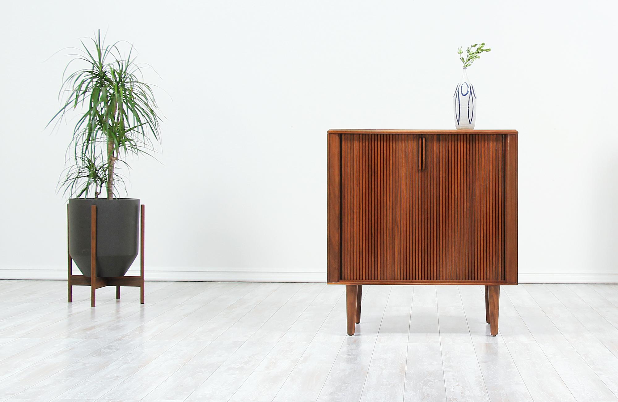 Minimalist vintage cabinet designed and manufactured in the United States by Barzilay, circa 1960s. Low in profile and compact in size, this stylish cabinet features a sturdy walnut wood frame with two tambour doors and four tapered legs that