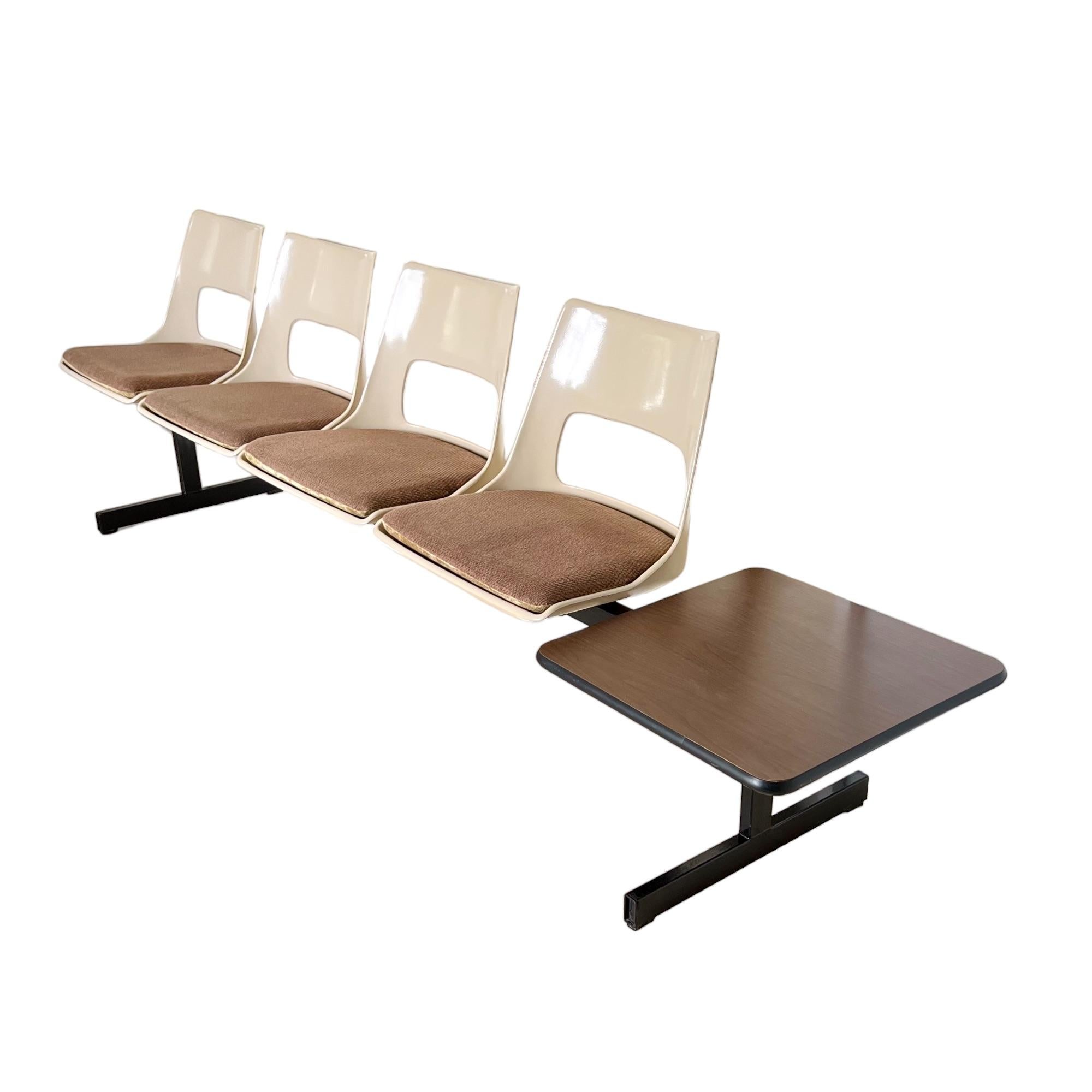 Vintage mid-century modern tandem beam seating by Krueger International circa 1970. This bench features four molded fiberglass light beige color shells and a wood finish side table connected on a black metal stretcher frame. The fiberglass seats are