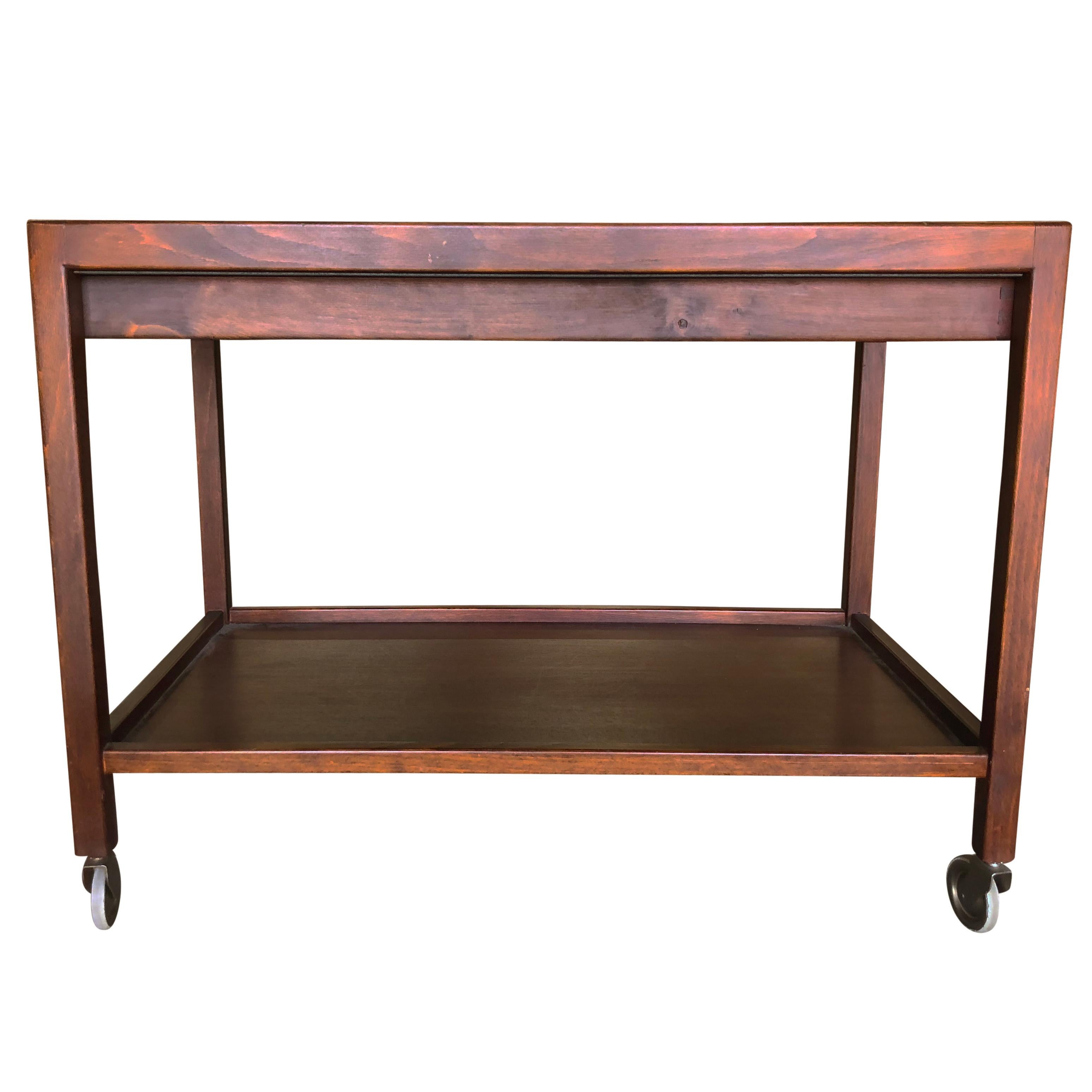 A dark-brown, vintage Mid-Century Modern tea trolley on steel wheels with a shelf and drawer, made of hand crafted Teakwood in good condition. The glass top of the Scandinavian coffee, side table is slightly smoked, supported by wood fittings. Wear