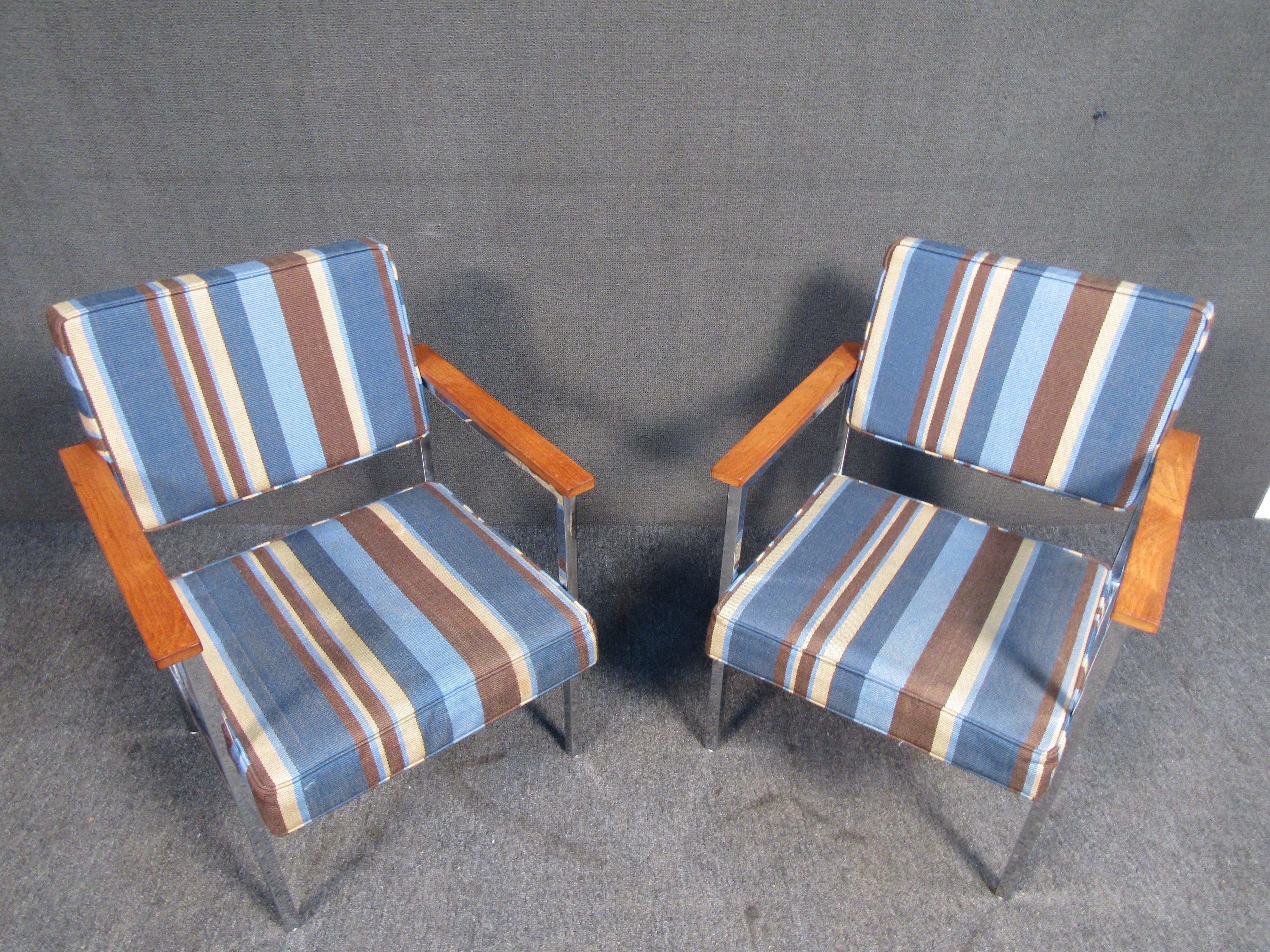 These unique club chairs feature rectangular teak arm rests on a sturdy metal frame. The stripped blue upholstery will compliment any setting you decide to pair them with. 
Please confirm item location with seller (NY/NJ).