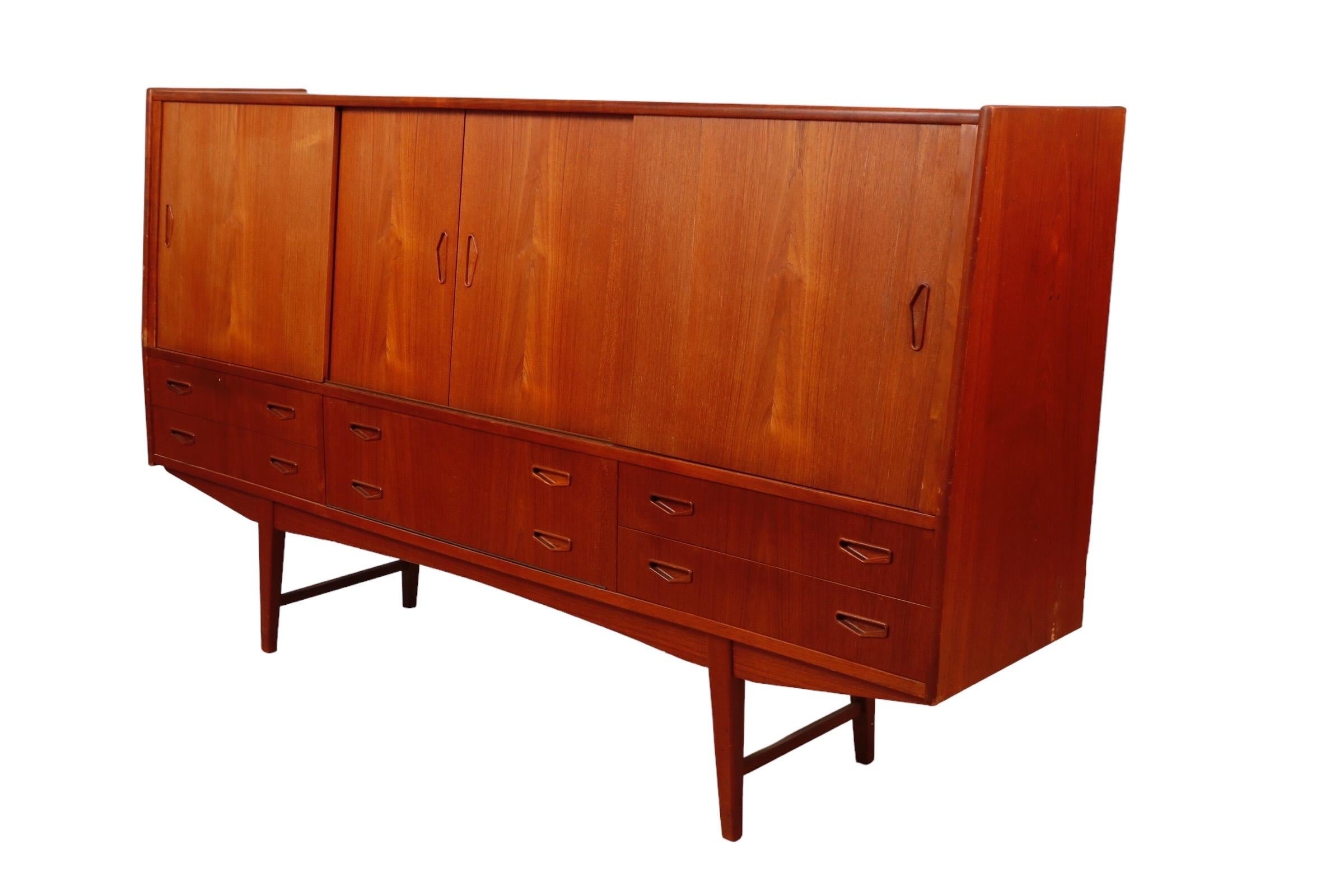 A 1960’s Danish teak bar sideboard. Lots of storage, cabinets flank a mirrored serving area with inlaid details on two central small drawers. Below four drawers and a drop front give the look of six with recessed handles.