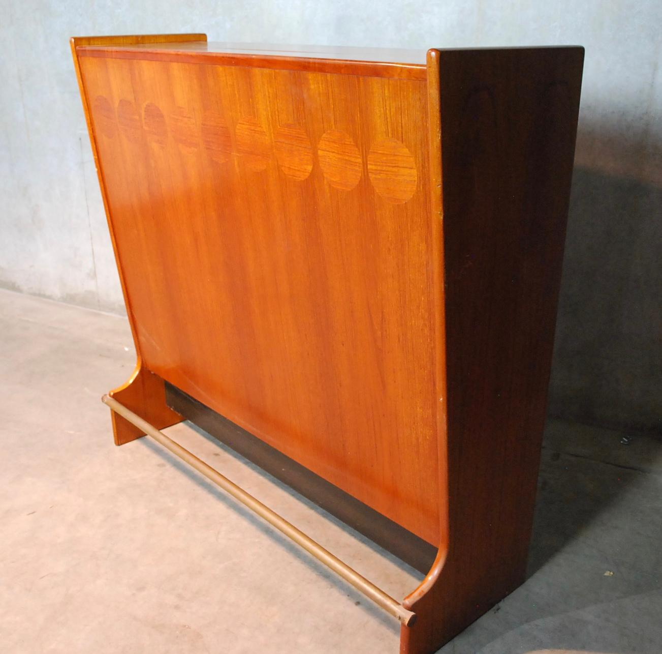 A stunning freestanding teak bar from the 1960s designed by Johannes Andersen for J. Skaaning & Son of Denmark. Beautifully decorated on both sides with cross grained elliptical marquetry and sculpted door pulls. Upper section flips and drops open