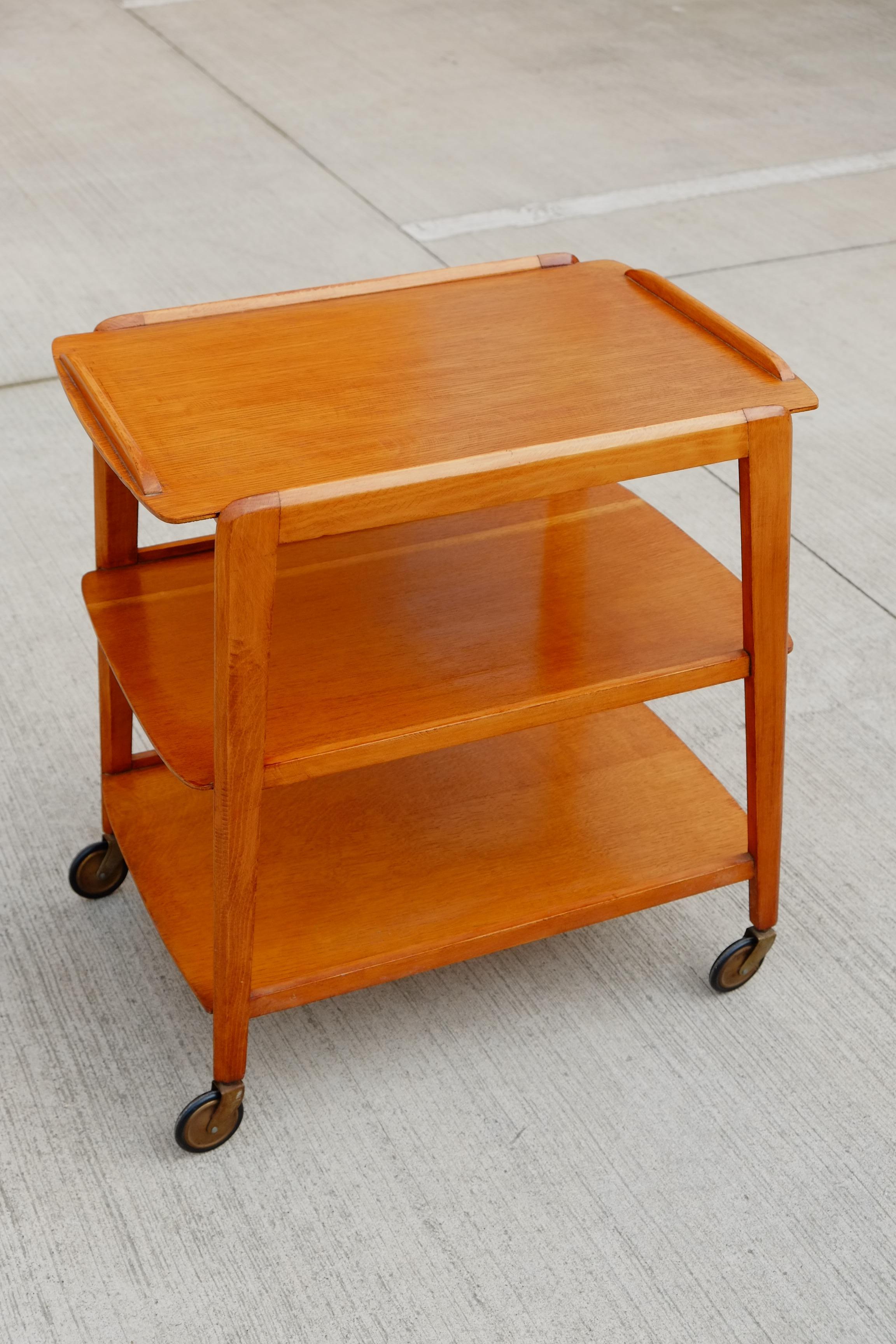 A nice Mid-Century Modern teak trolley cart from the 1960s. The trolley has a gorgeous angular shape which is wider at the bottom and narrows to the table top. angular lipped trays in a rich teak colour wood. Large rubber wheels. A stylish serving