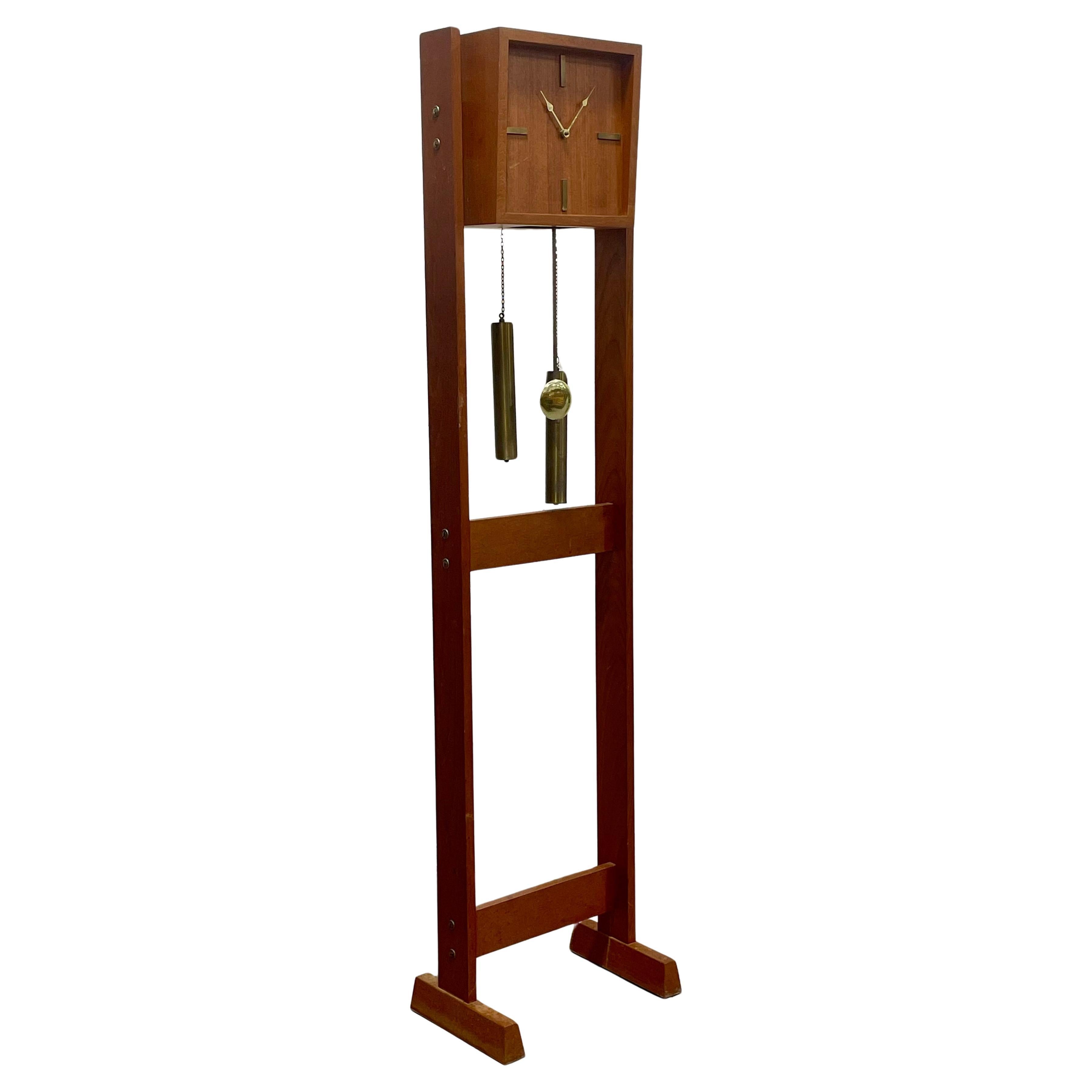 Mid Century Modern Floor Clock featuring a solid teak case with minimalist brass accents and a sculptural open frame design. The clock showcases a clean square teak face with inset brass hour markers and hands, paired with a German-made