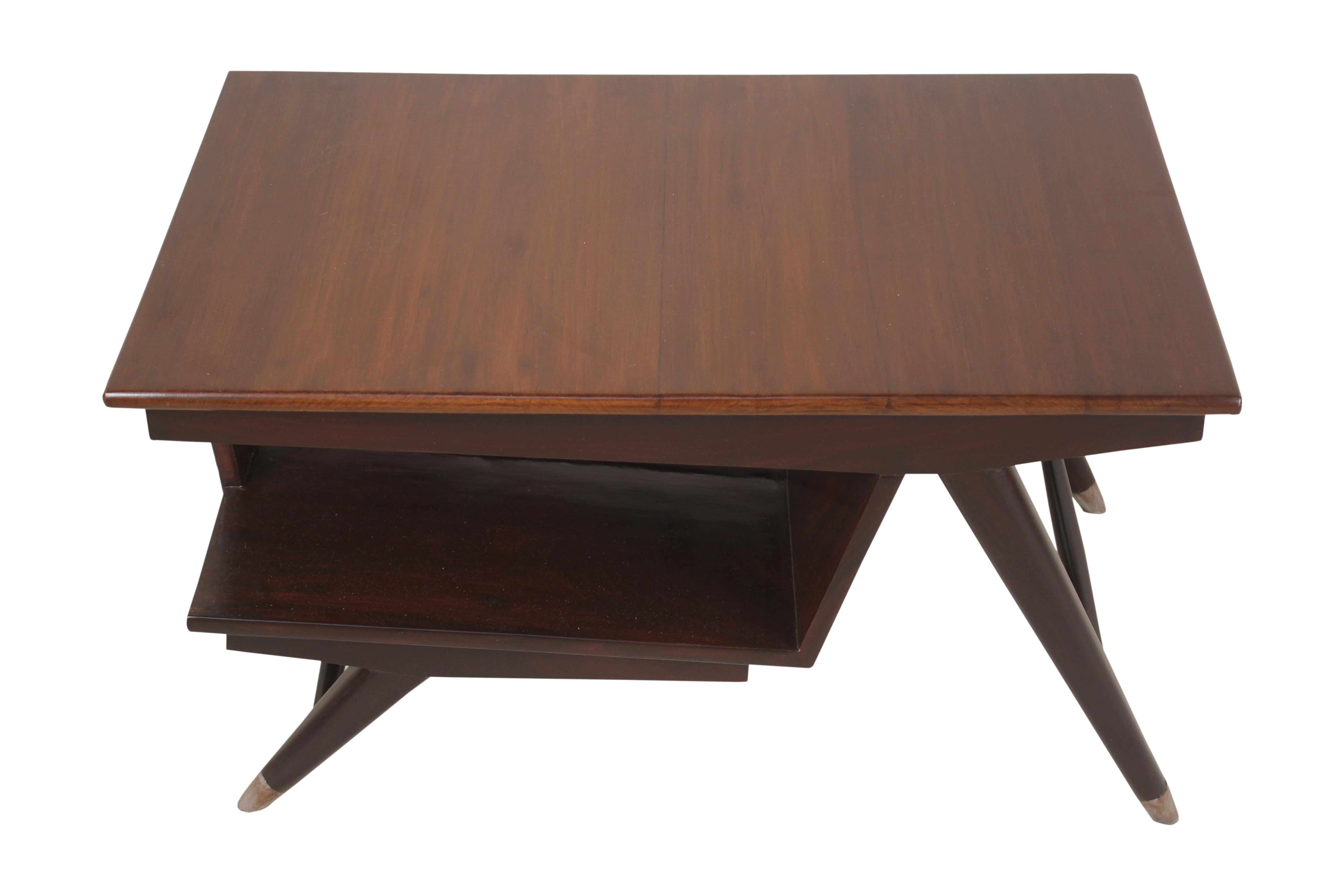 Mid-Century Modern teak coffee or cocktail table with an angled lower shelf for magazines or books. Brass feet on splayed legs and a carved harlequin design side support.