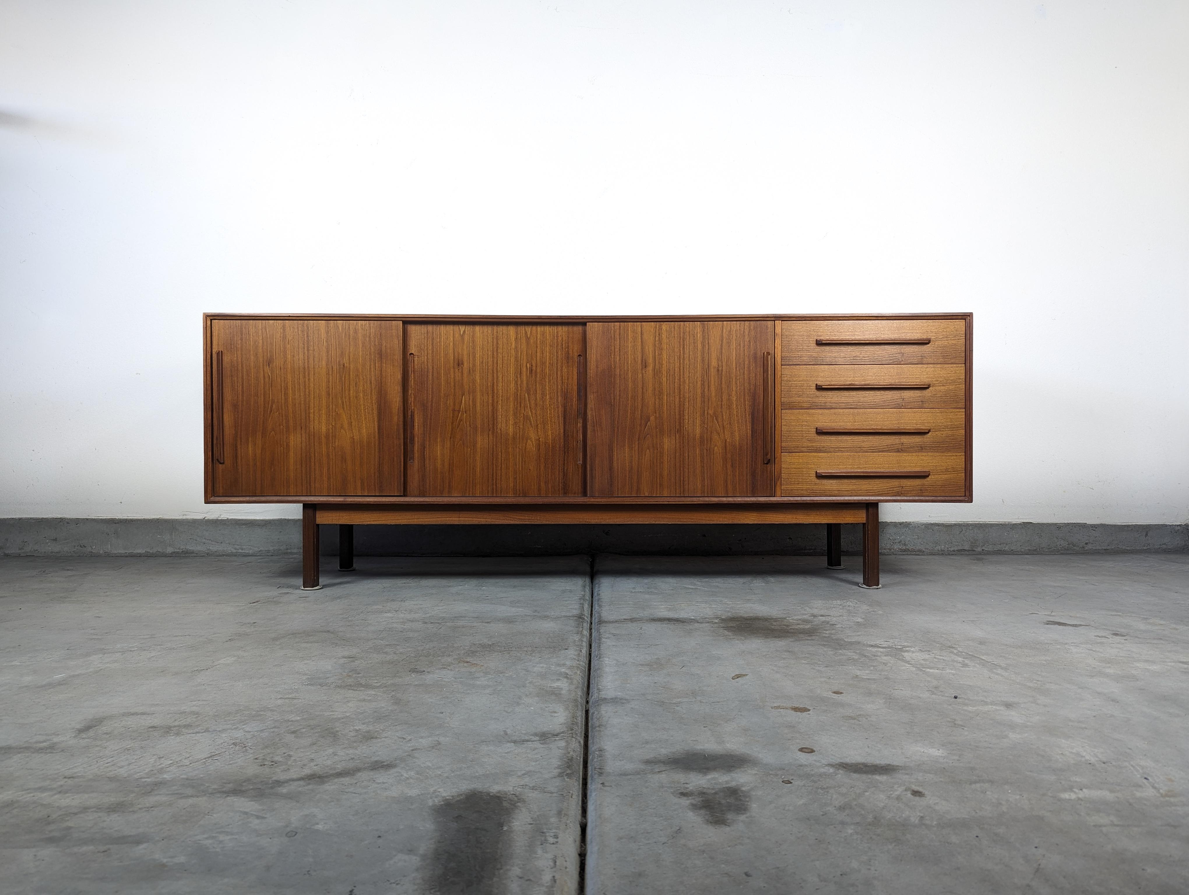 Immerse yourself in the epitome of mid-century sophistication with this exquisite Teak credenza, a true testament to the visionary design of Ib Kofod Larsen for Faarup Mobelfabrik, hailing from the vibrant creativity of the 1960s. This credenza,