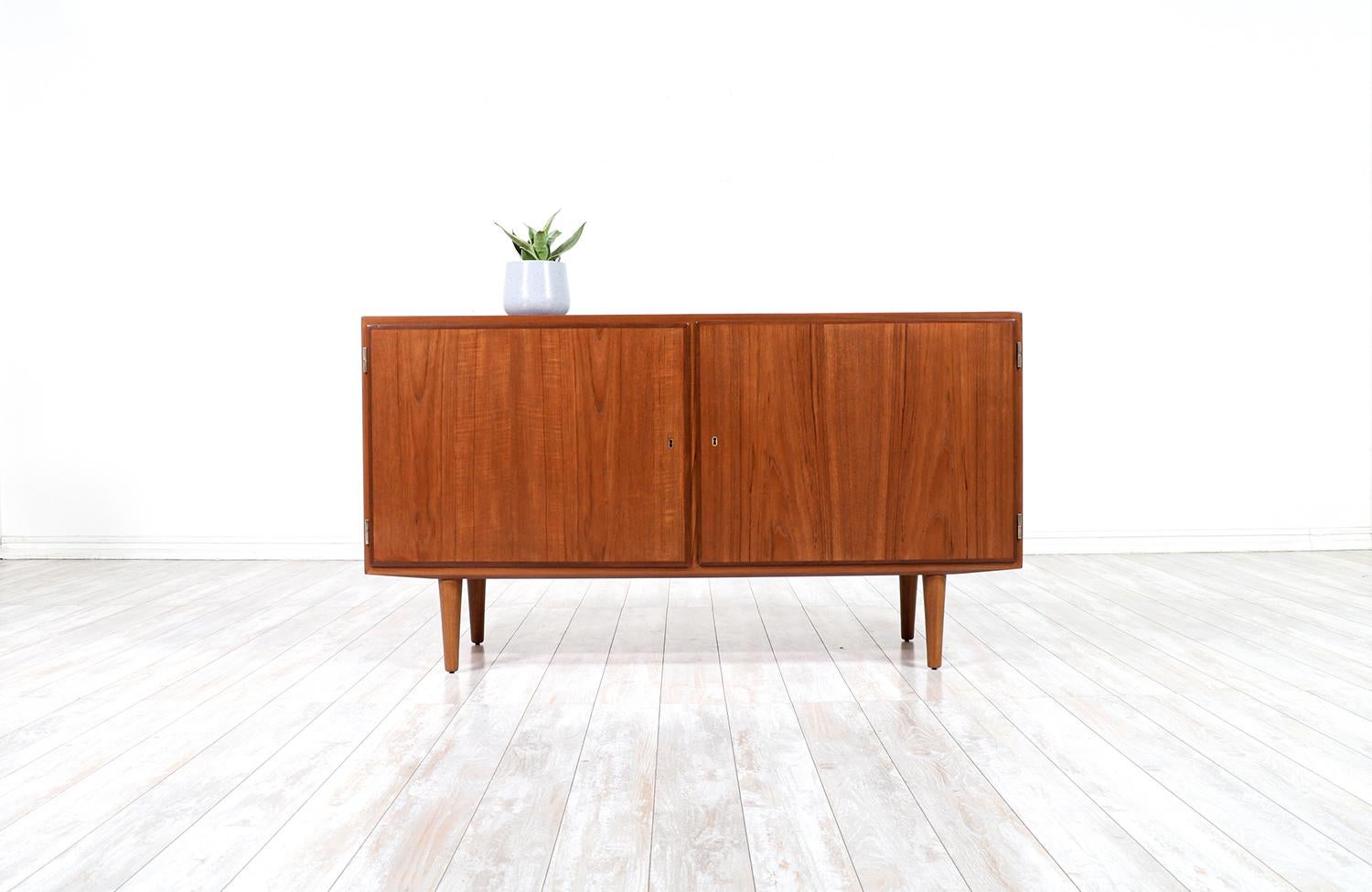 Danish Modern credenza designed by Carlo Jensen for Hundevad Co. in Denmark circa 1960’s. This compact credenza includes tapered solid teak wood legs and two doors with a vintage key and keyhole mechanism to keep your belonging safe and private when