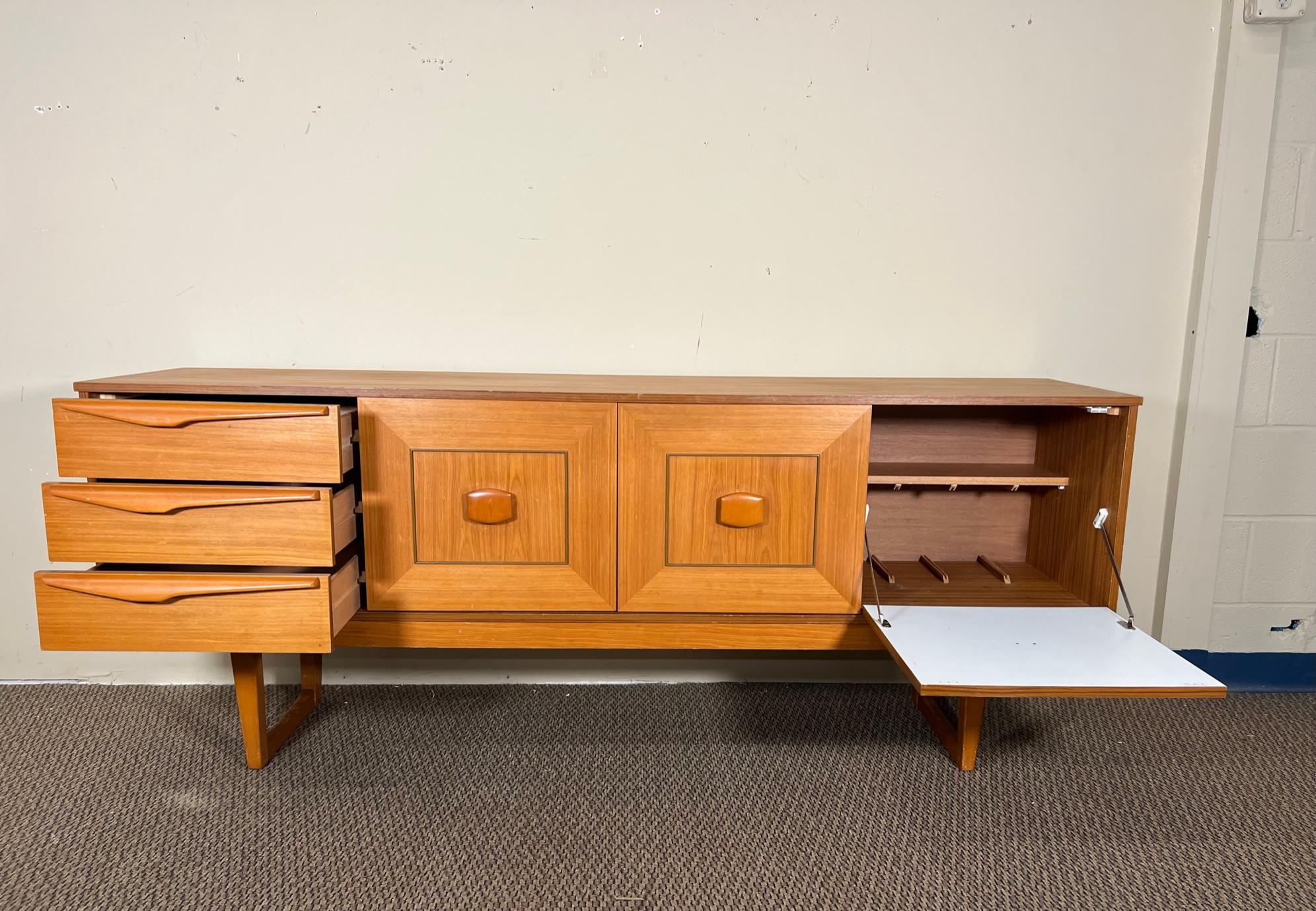Light wood credenza by Stateroom. Made in England.

Featuring sculpted handles and a drop down door bar cabinet. Very good condition overall. Some marks and scratches. Stains in bottom drawer, paint spots on the right side. Some dividers added