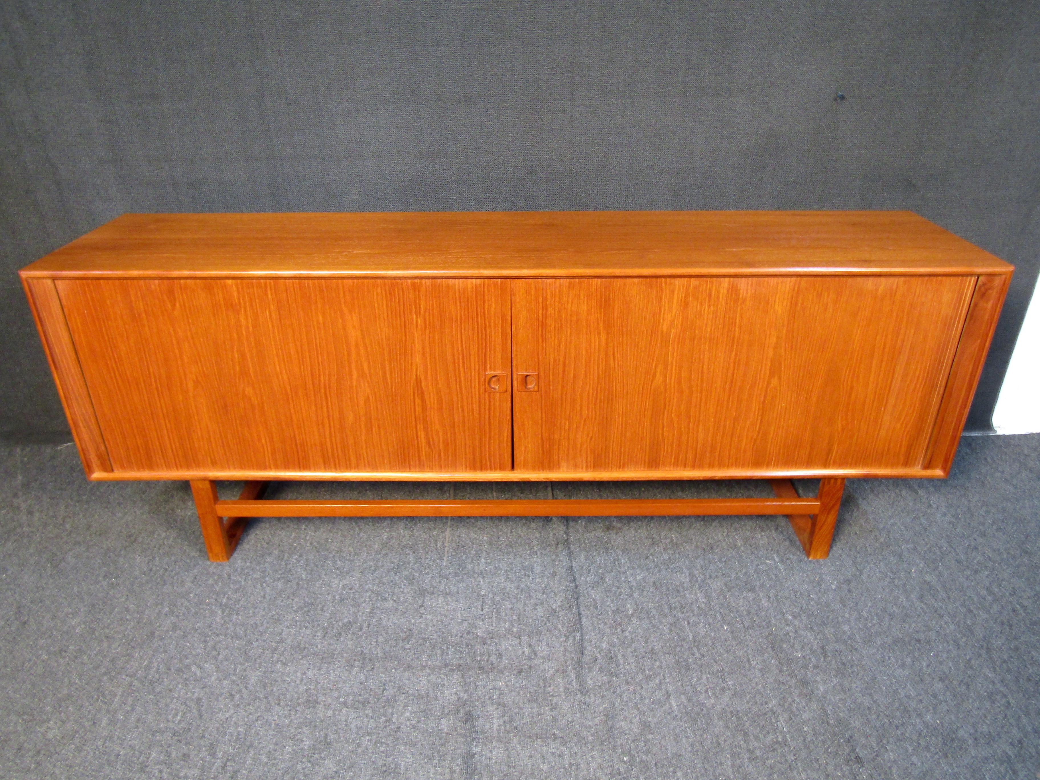 This stunning Danish Modern tambour sideboard features a beautiful teak finish, and spacious interior cabinet space. Multiple shelves and a lined center drawer that makes this a versatile storage piece for any Mid-Century setting. Made in Denmark,