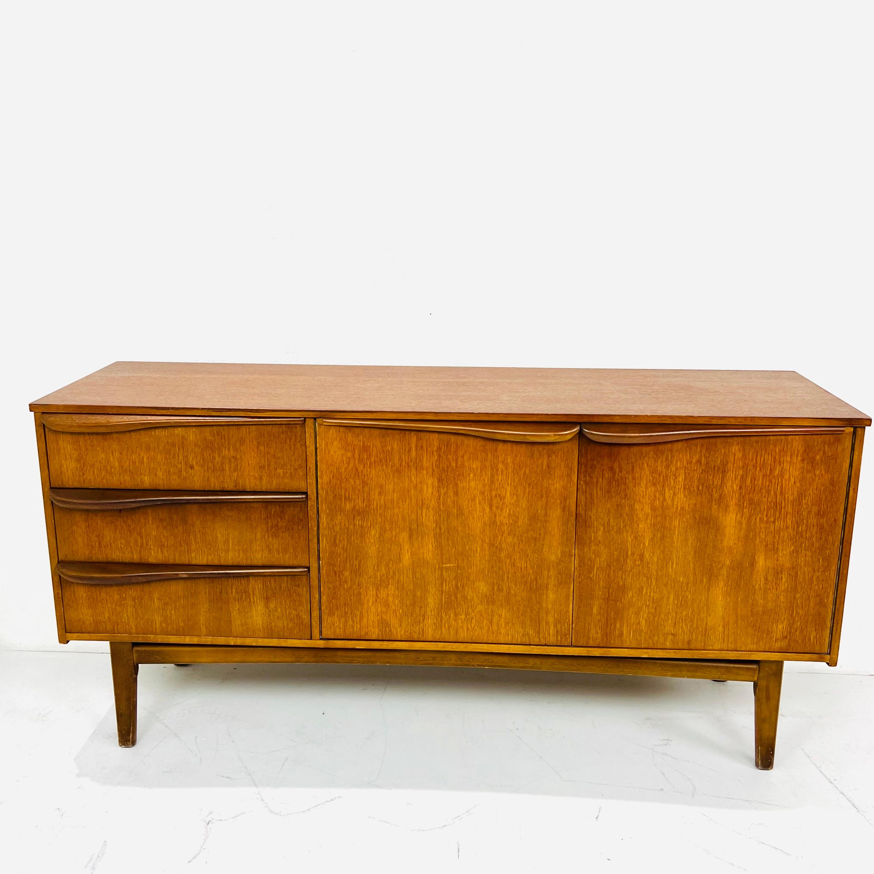 Sculptural Mid Century Modern teak Credenza / Sideboard. Ample storage space with three drawers and two spacious shelving areas. The hand-pulls are set asymmetrically on the drawers which adds to the funky styling of this piece.
Very good vintage