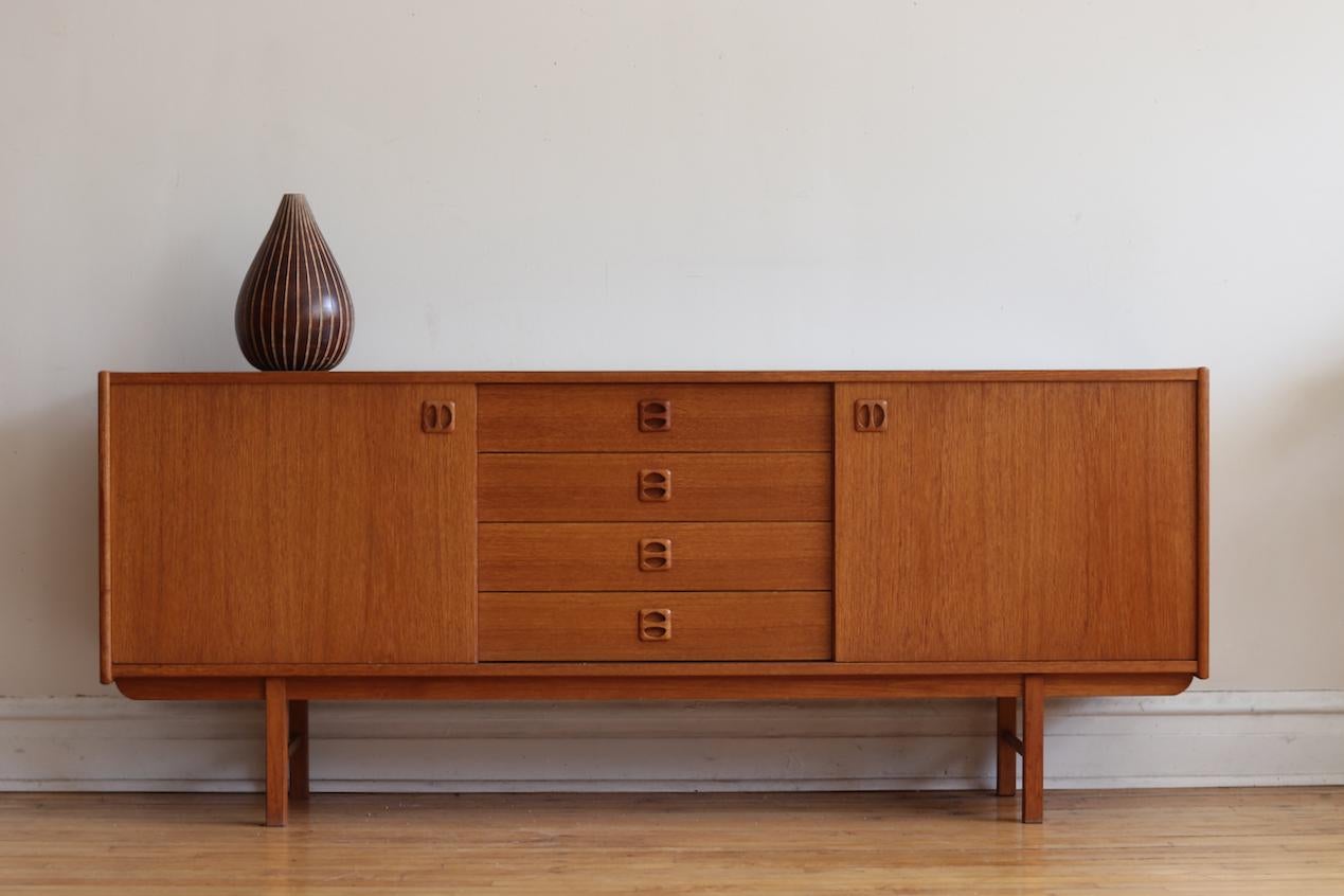 Midcentury Danish modern teakwood sideboard.
Just imported from Denmark and refinished!
Four dovetailed drawers in the center flanked with sliding cabinet doors.
Cabinets hold removable shelving.
Excellent vintage condition!

Measures: 72”