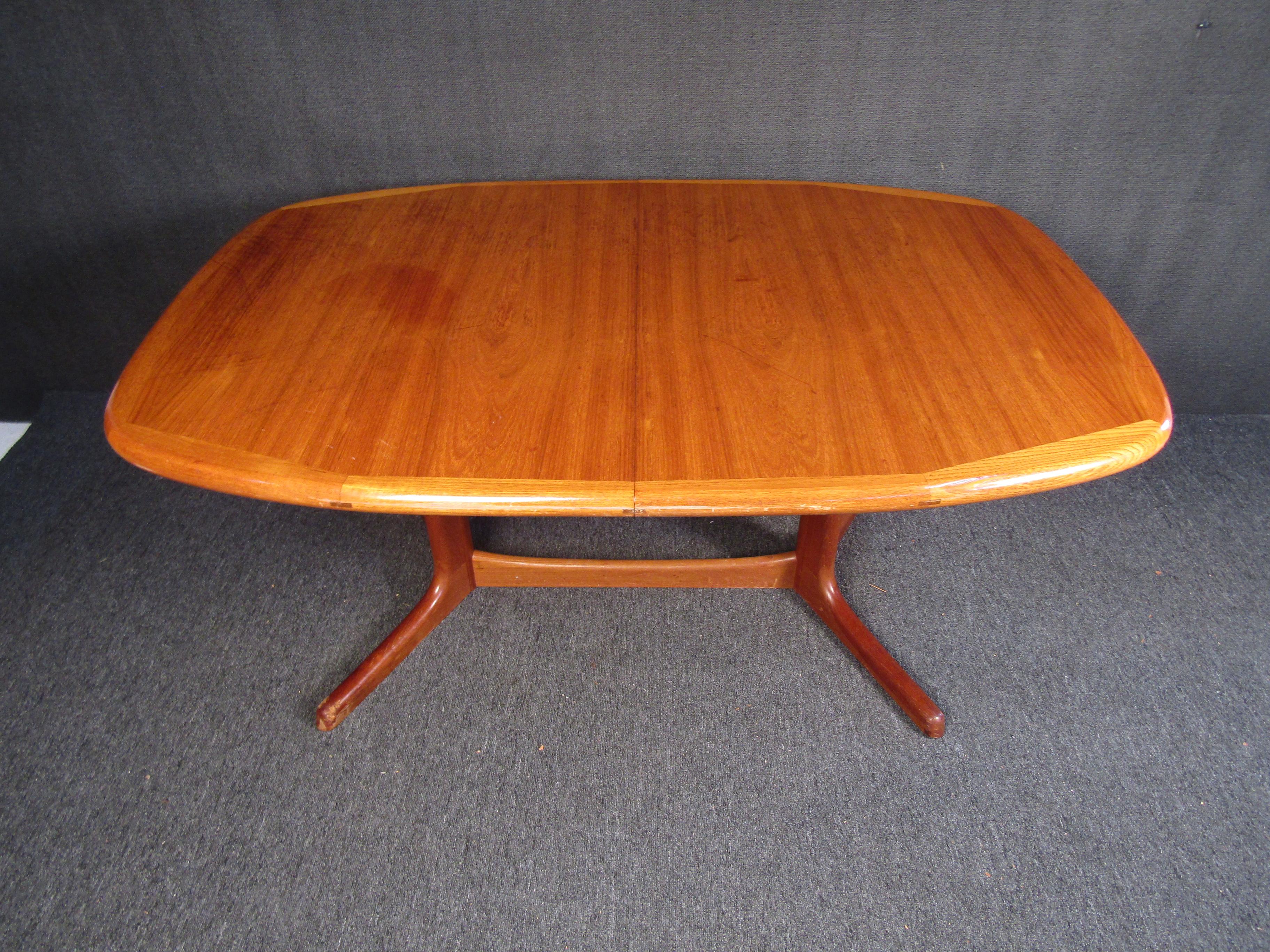 Showing off a rich teak woodgrain, this Mid-Century Modern dining table can add subtle flair to a dining room through its elegant, minimal design. Please confirm item location with seller (NY/NJ).