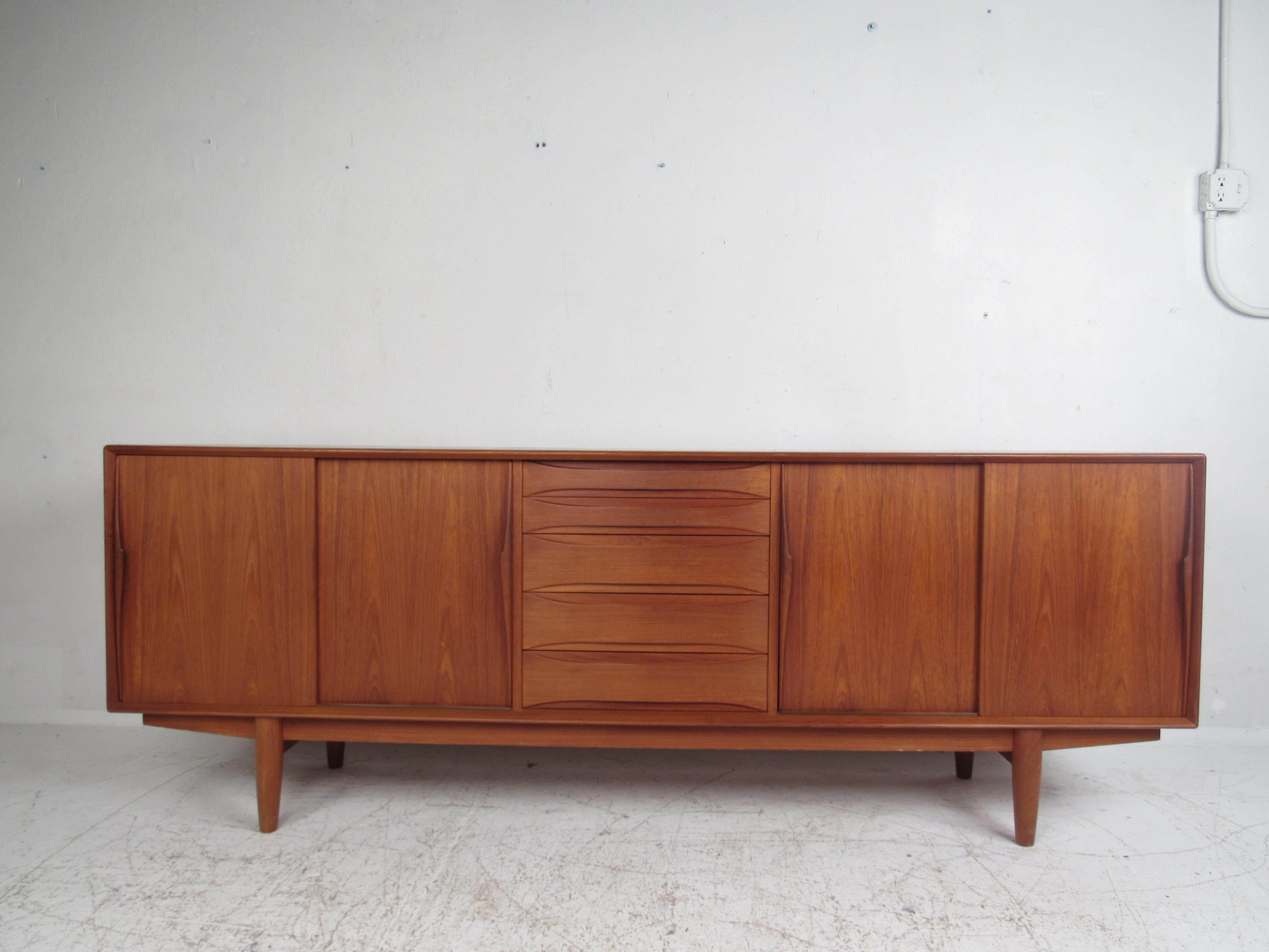 This stunning vintage modern sideboard features oval recessed drawer pulls and convenient sculpted door handles. A sleek design that offers plenty of room for storage within its many drawers and large compartments hidden by sliding doors. The rich