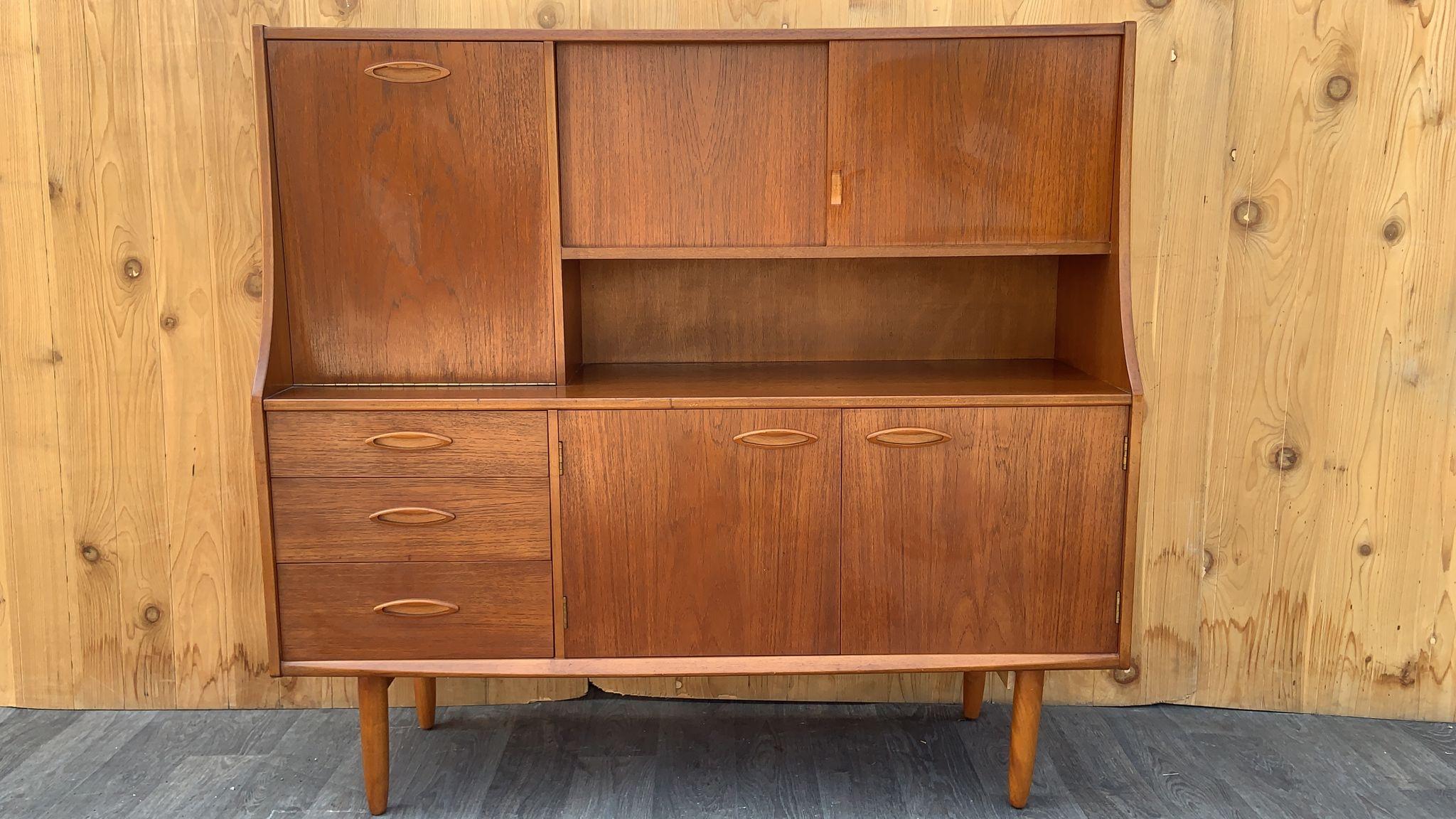 Mid Century Modern Teak Highboard by Jentique 

This Teak Mid Century Modern highboard was produced by Jentique. This highboard has a drop front bar and sliding door cupboard up top, and the base has three drawers and a double-door cupboard. This is