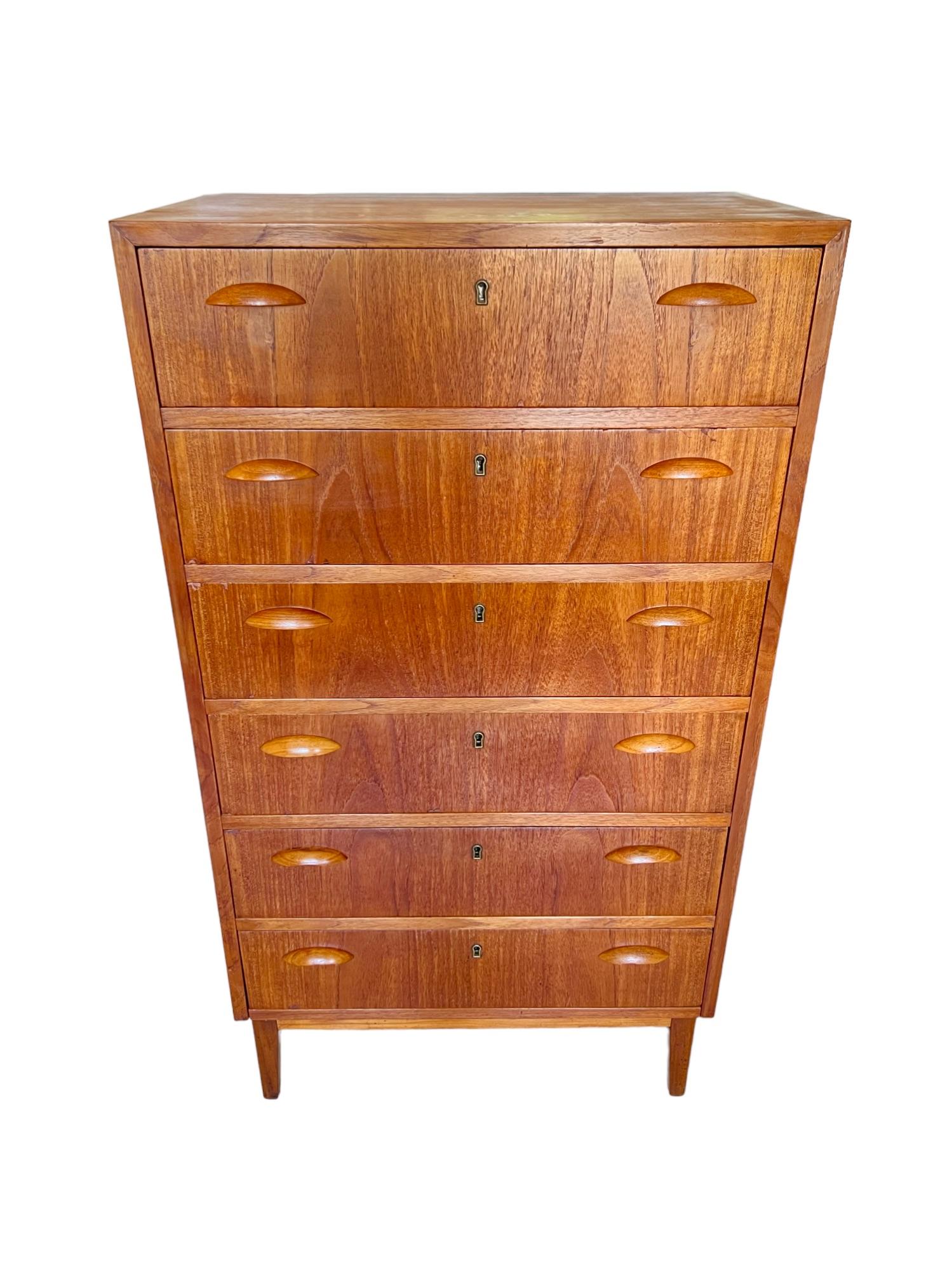 This vintage 1950s mid-century modern highboy dresser features six locking (no key) drawers with sculpted cup pulls and superb dovetail joinery. Constructed of hardwood and teak veneer, it is a relatively lightweight and petite tall chest. It is