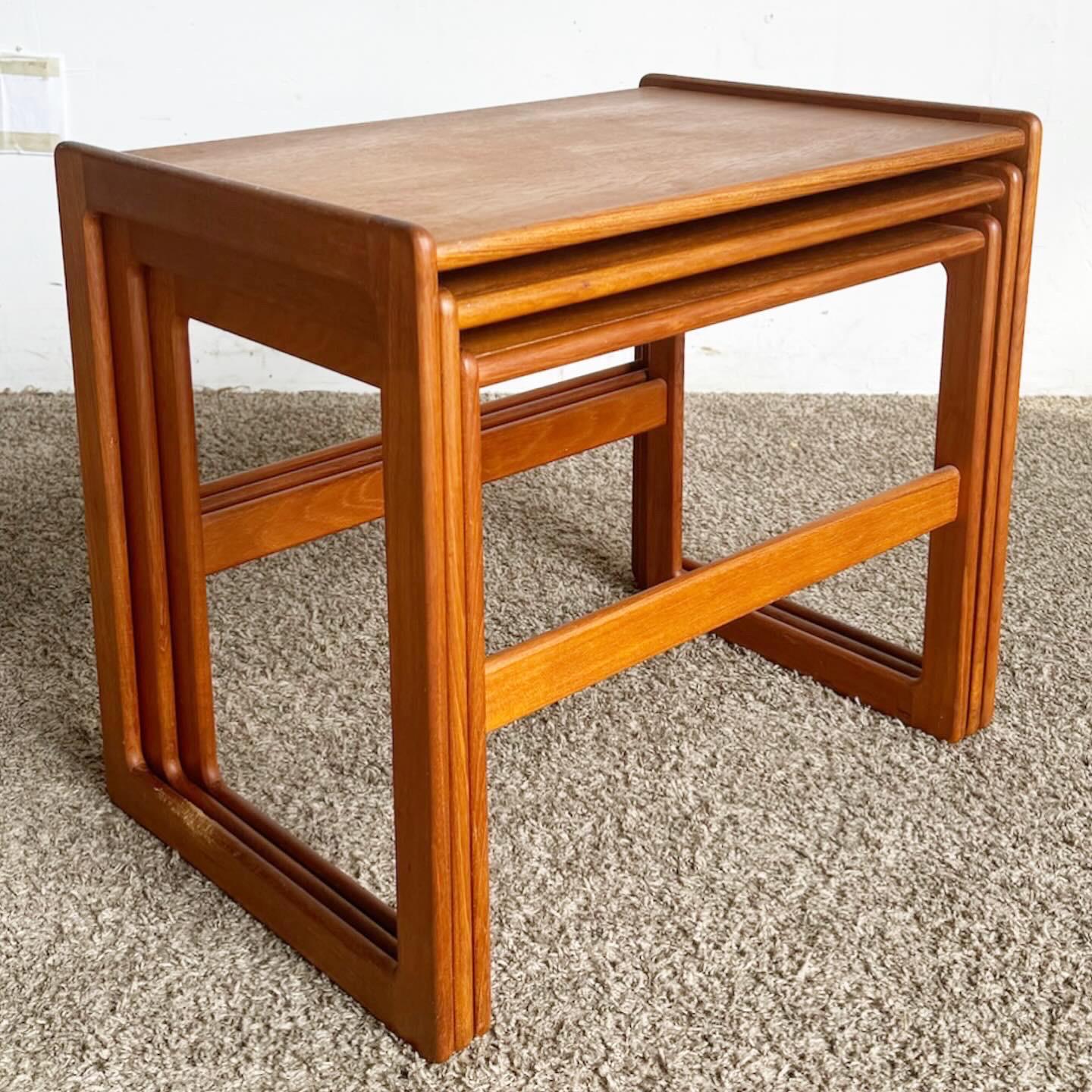 The Mid Century Modern Teak Nesting Tables, a set of three, offer stylish versatility in classic mid-century design. Made from high-quality teak, they feature a natural grain, enhancing any room with organic beauty. The set includes three sizes,